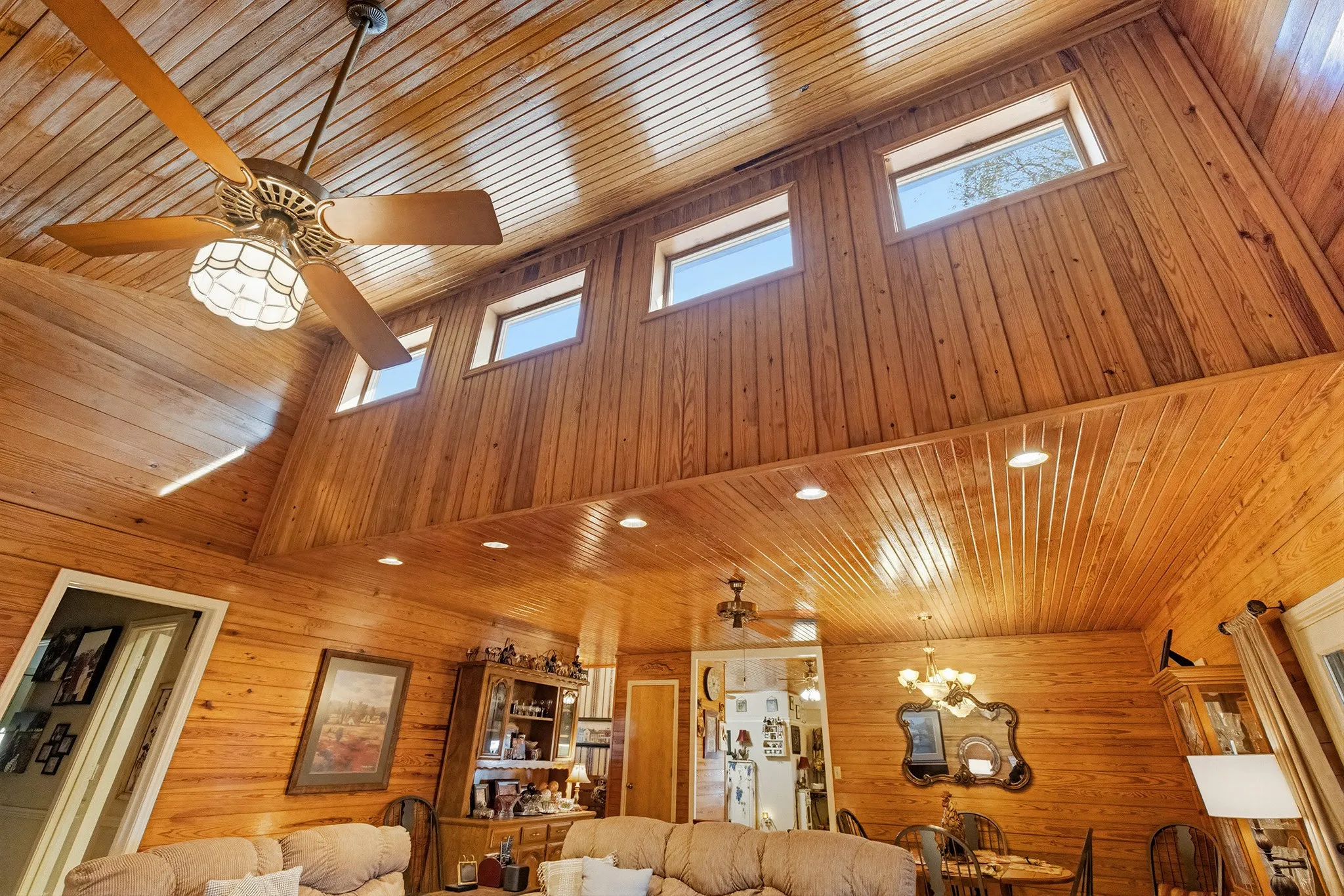 Living room with a ceiling fan, a vaulted wood ceiling, wood walls, and recessed lighting