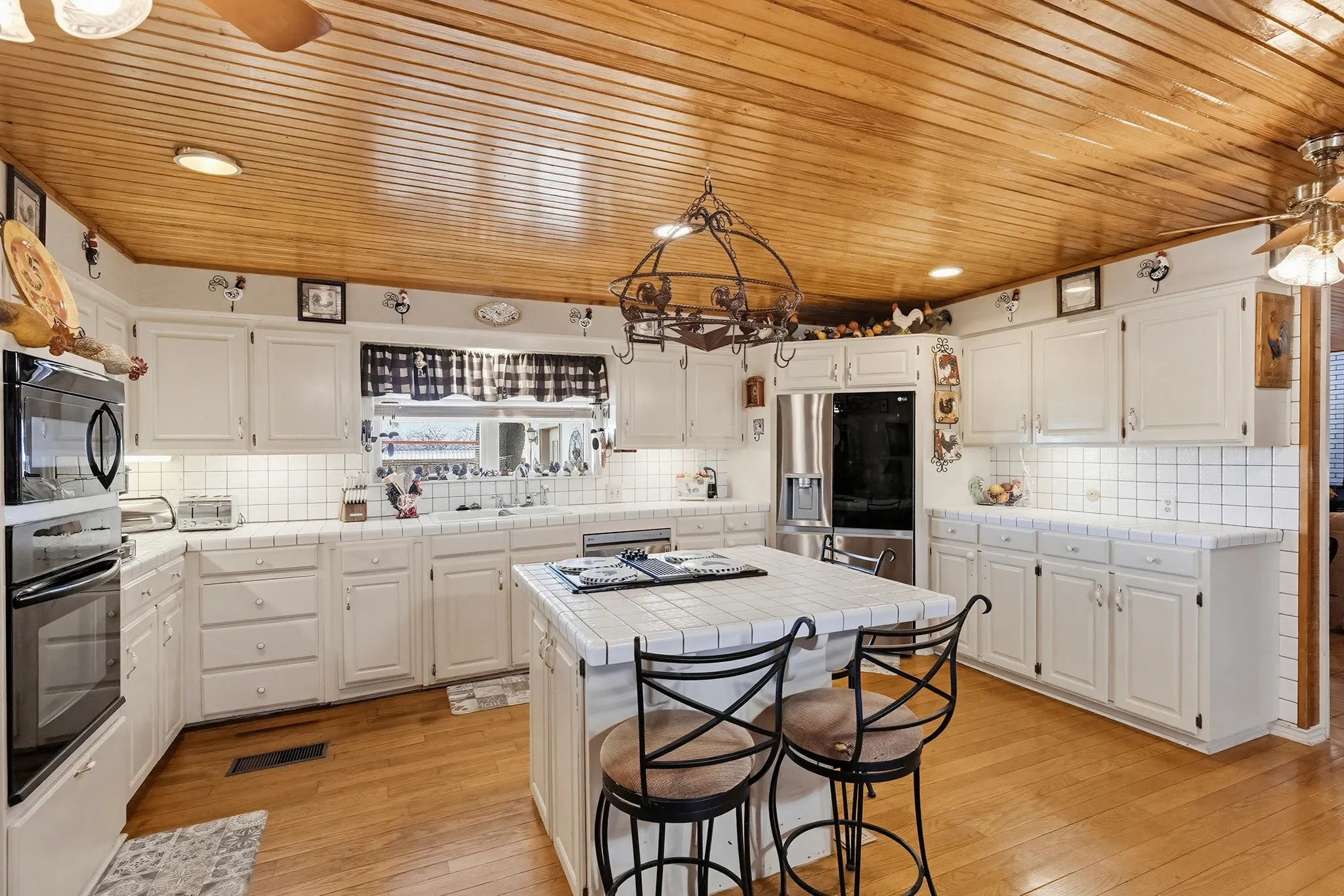 Kitchen with tile countertops, a breakfast bar area, black appliances, tasteful backsplash, and a center island