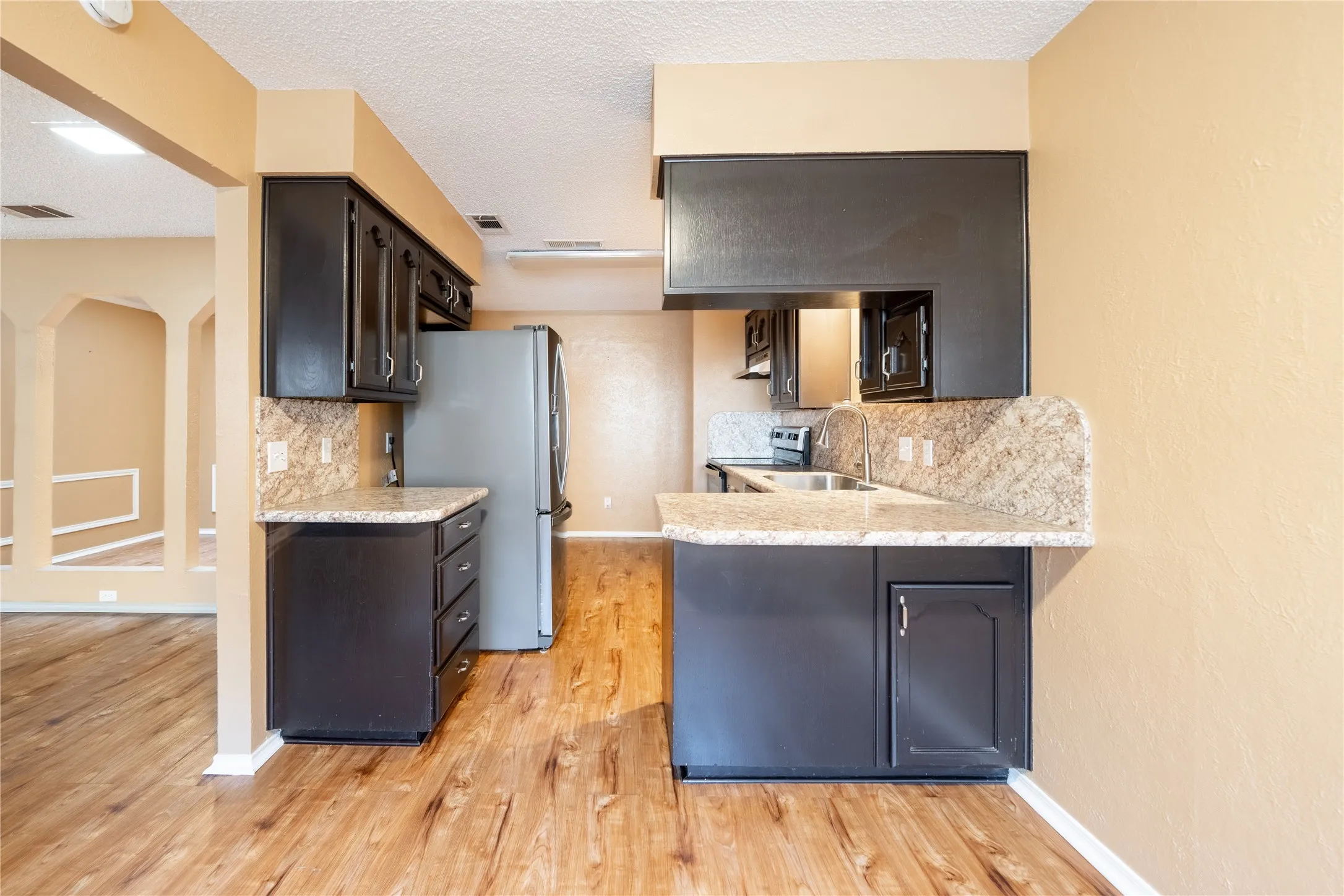 Kitchen with tasteful backsplash, arched walkways, a sink, light wood-style floors, and stainless steel appliances