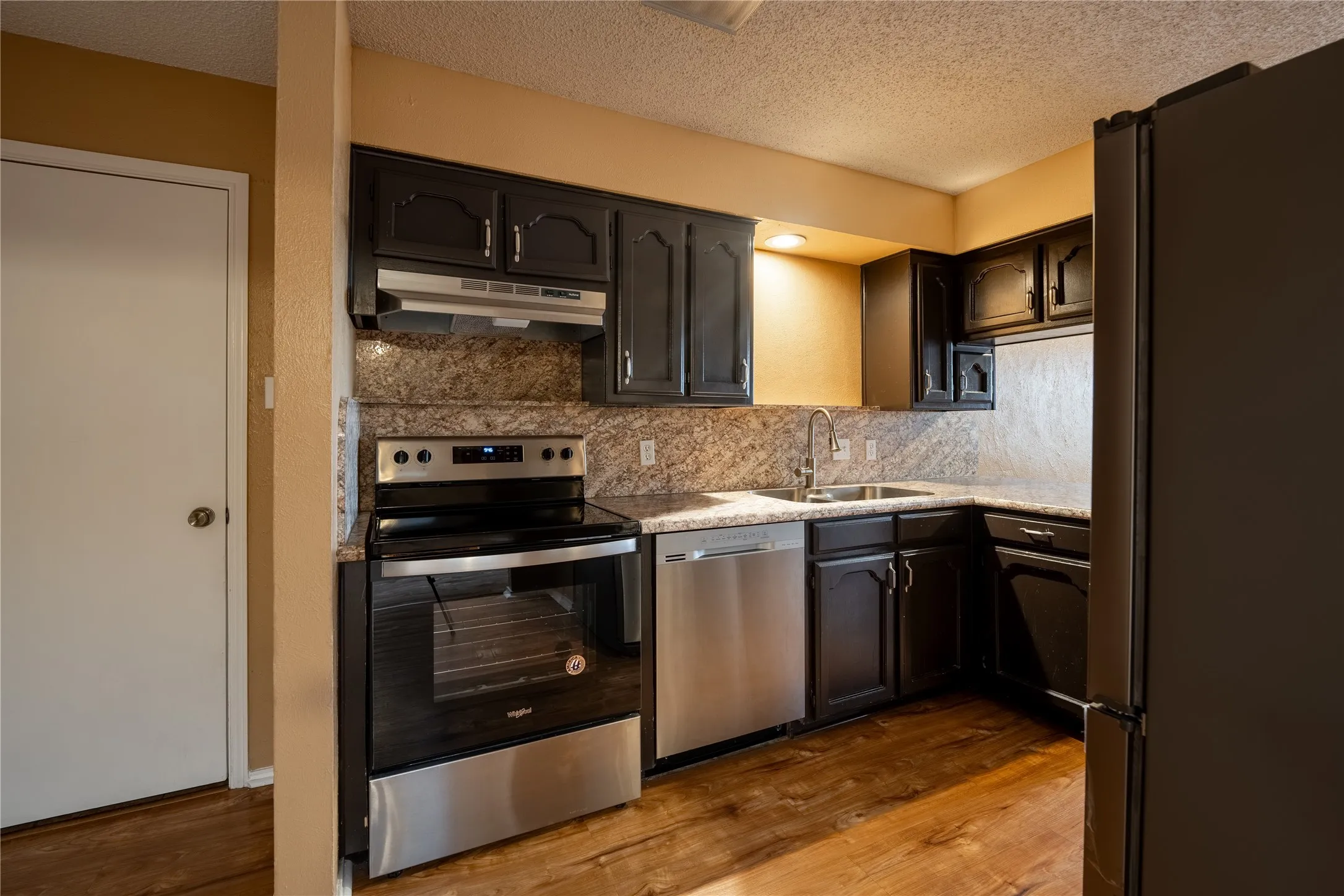 Kitchen with wood finished floors, under cabinet range hood, a sink, and appliances with stainless steel finishes