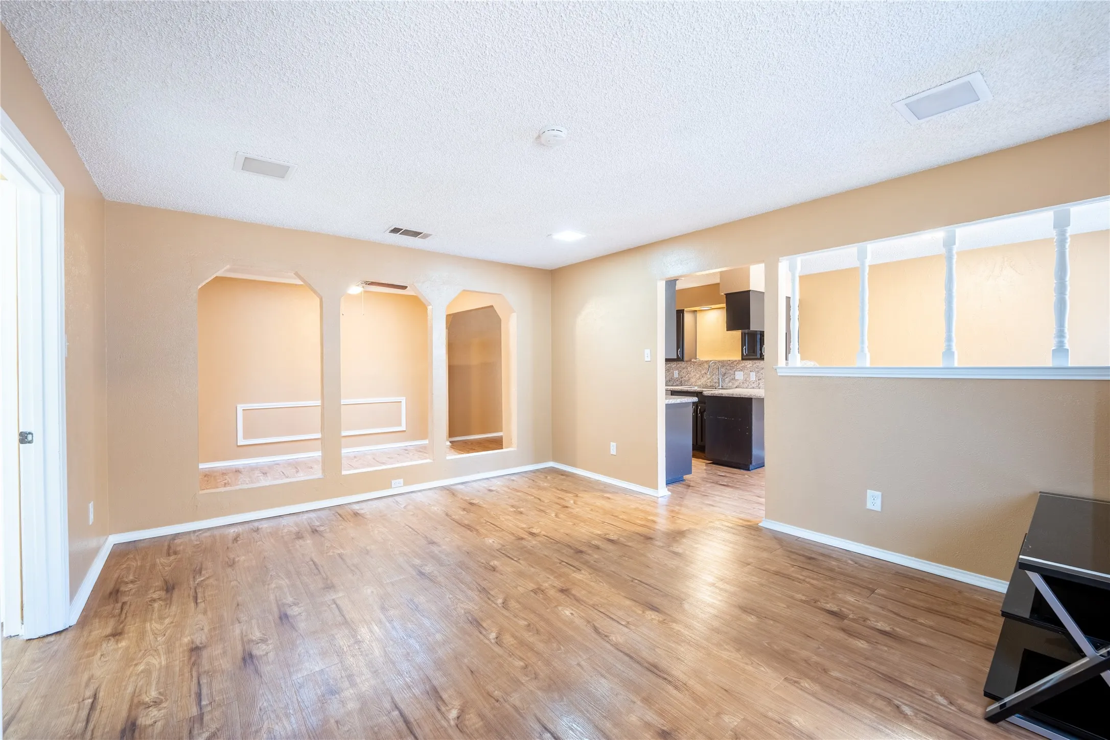 Unfurnished living room with light wood-style flooring, arched walkways, baseboards, and a textured ceiling