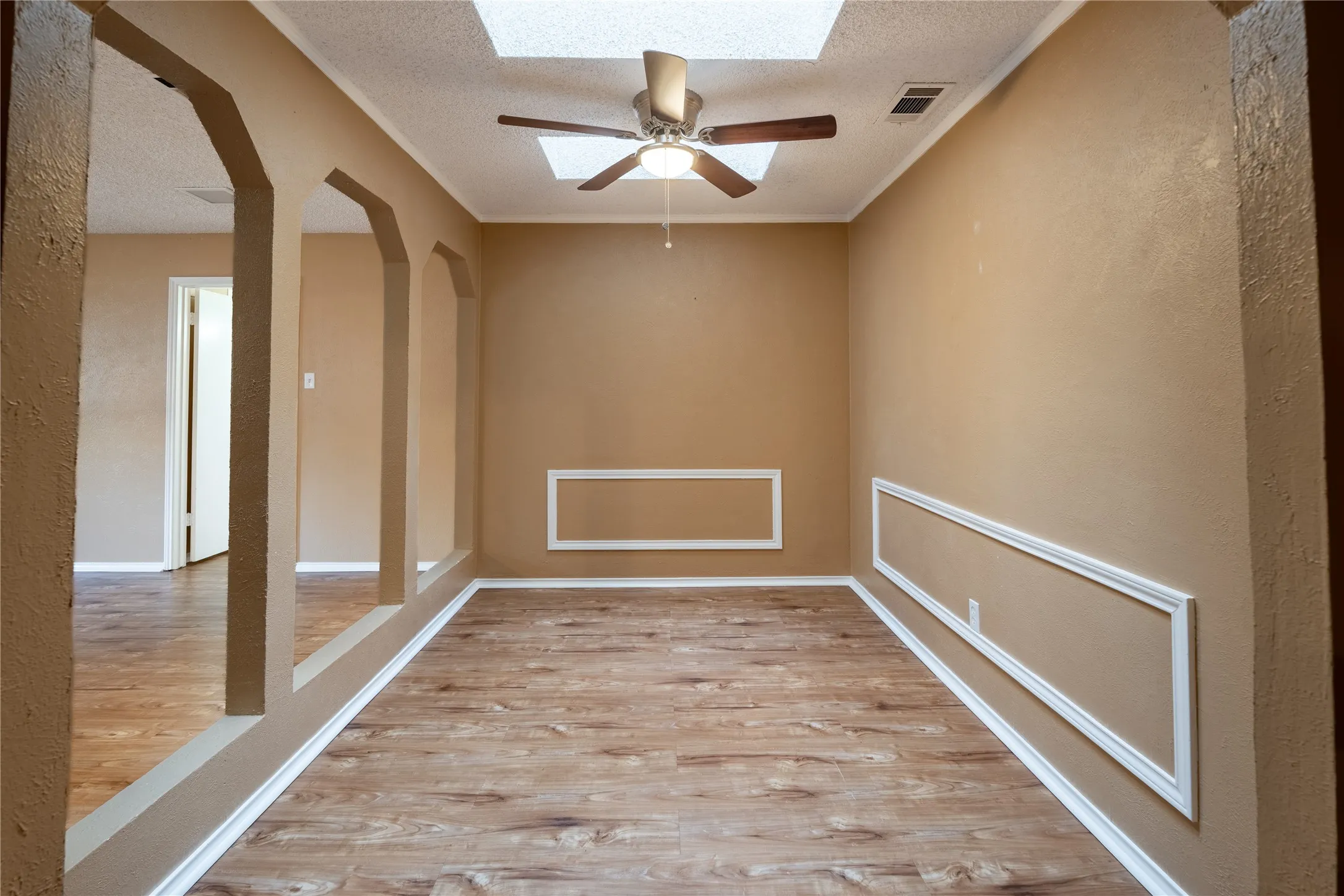 Empty room with crown molding, a textured ceiling, arched walkways, visible vents, and wood finished floors
