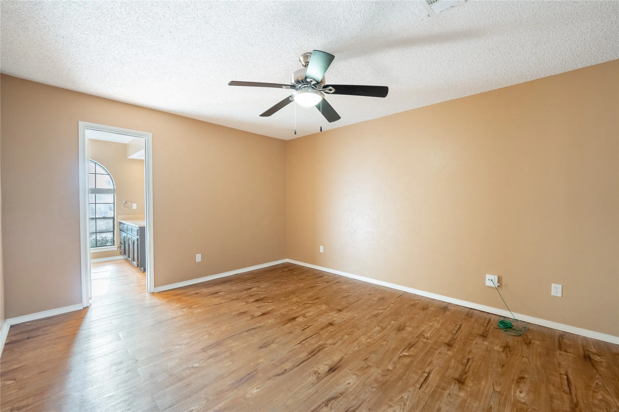 Empty room with light wood-style flooring, a textured ceiling, ceiling fan, and baseboards