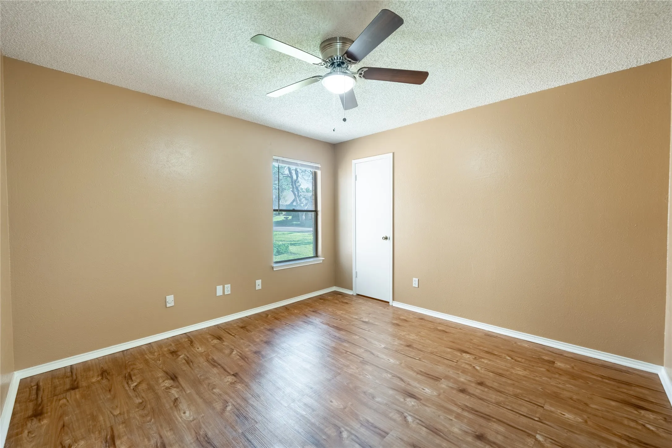 Unfurnished room featuring a textured ceiling, baseboards, a ceiling fan, and wood finished floors