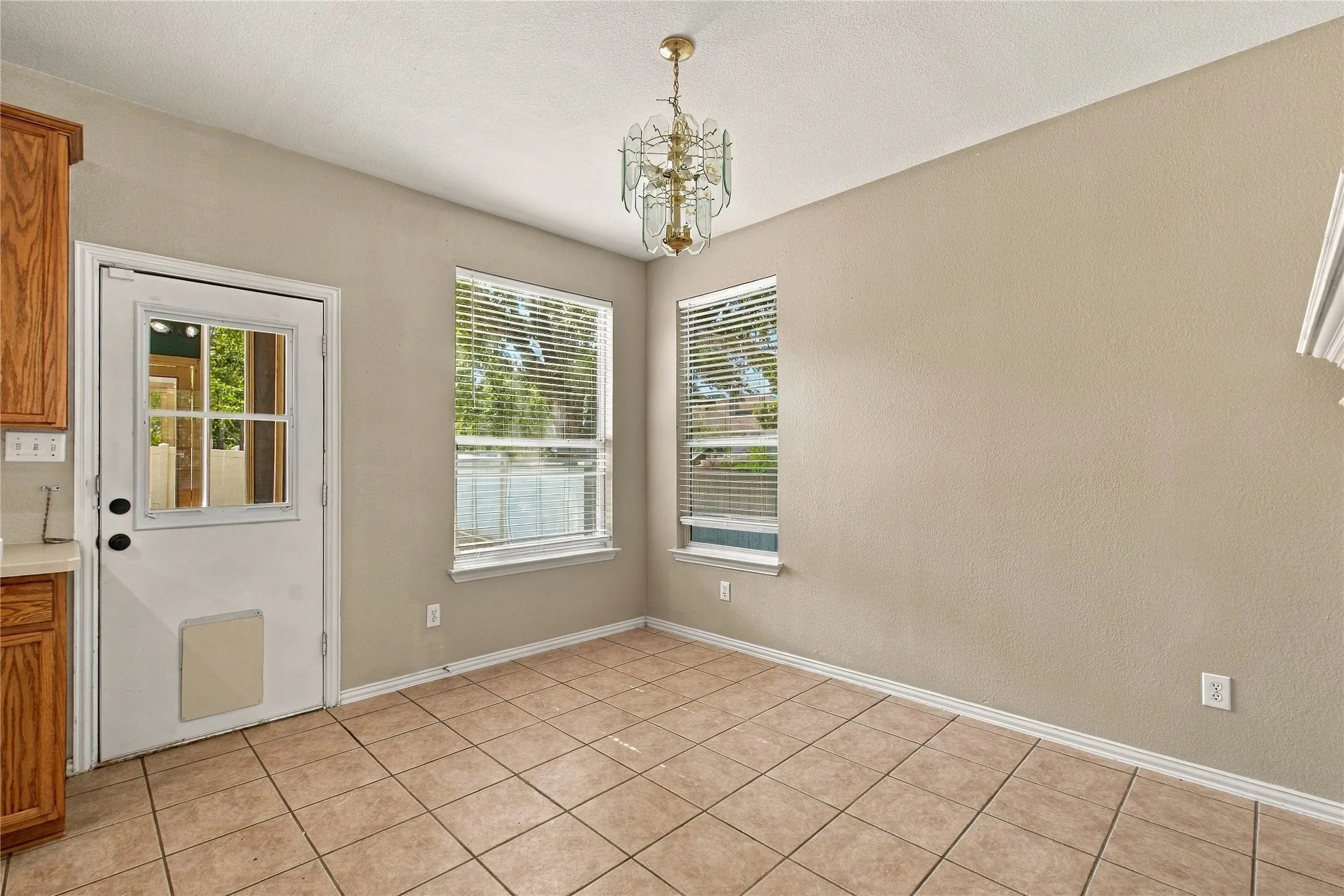Tile flooring, neutral wall tones, two windows with blinds, a glass-paned exterior door, and a decorative ceiling light fixture
