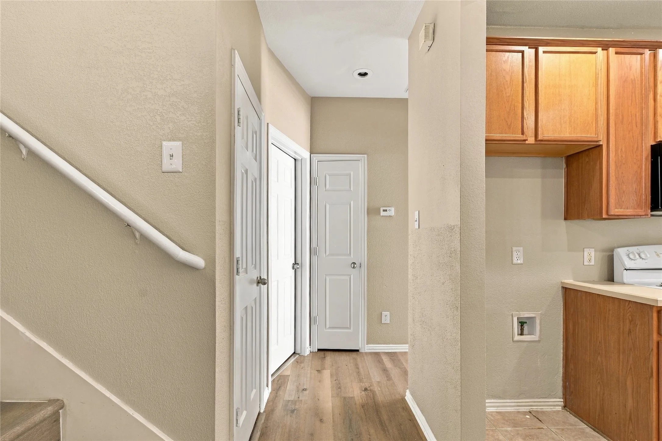 Wood-finish flooring, staircase with handrail, paneled doors, and wood cabinetry