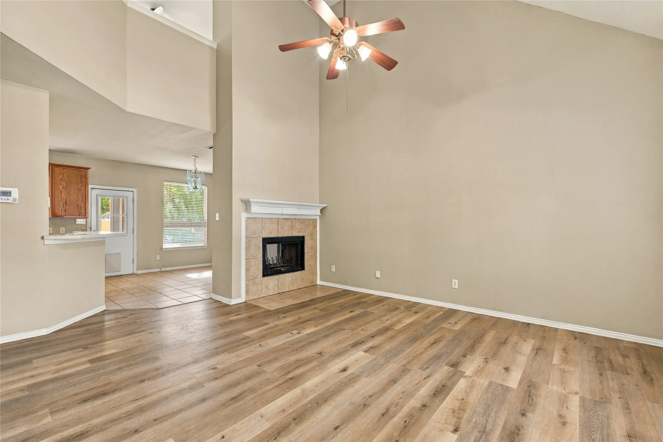 Vaulted ceiling with ceiling fan, wood-finish flooring, fireplace with tile surround and mantel, and kitchen with wood cabinetry