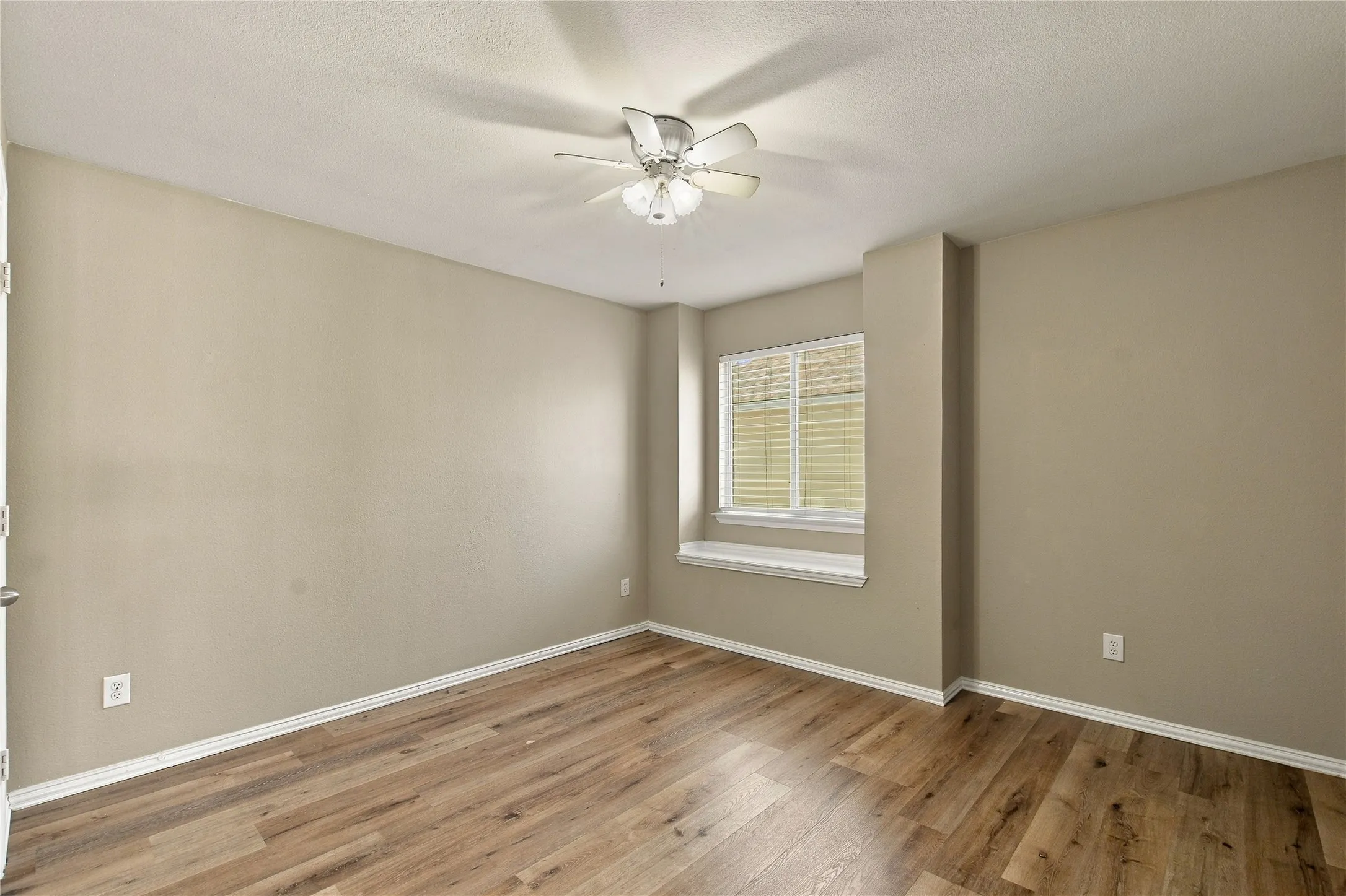Wood-finish flooring, neutral wall tones, window with horizontal blinds, ceiling fan with integrated lighting
