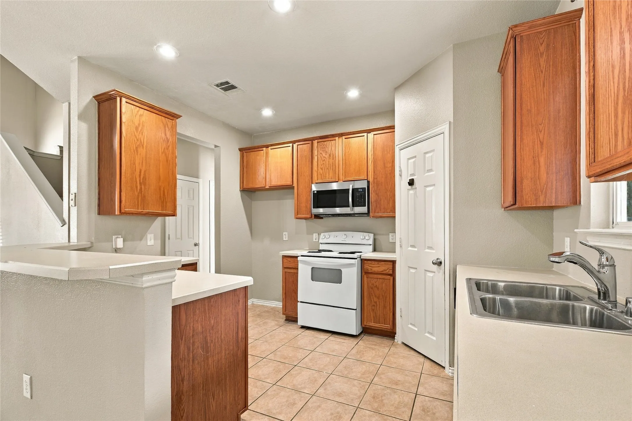 Kitchen featuring wood cabinetry, stainless steel microwave, white range, tile flooring, and a double basin sink
