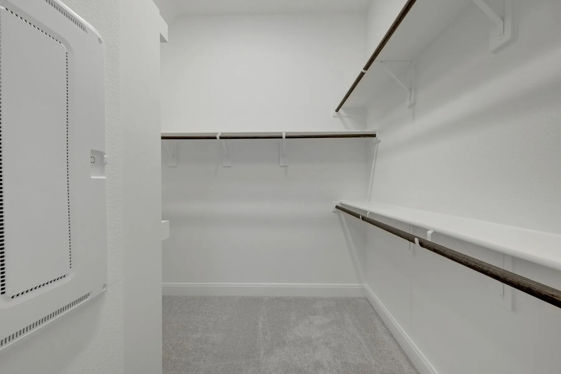 Walk-in closet featuring light gray carpet flooring, white walls, and built-in shelving with hanging rods