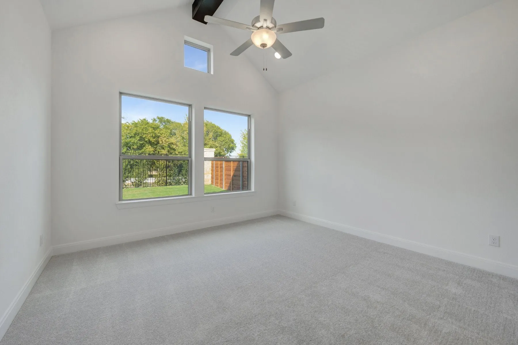 Vaulted ceilings and light gray carpeting, complemented by multiple windows and a ceiling fan with integrated lighting