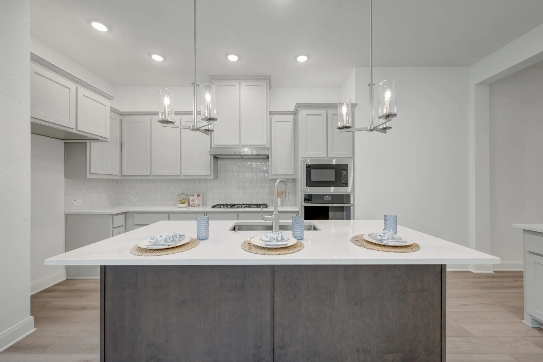 Kitchen featuring a large central island with a light-toned countertop, white cabinetry, integrated stainless-steel appliances, recessed lighting, and wood-finish flooring