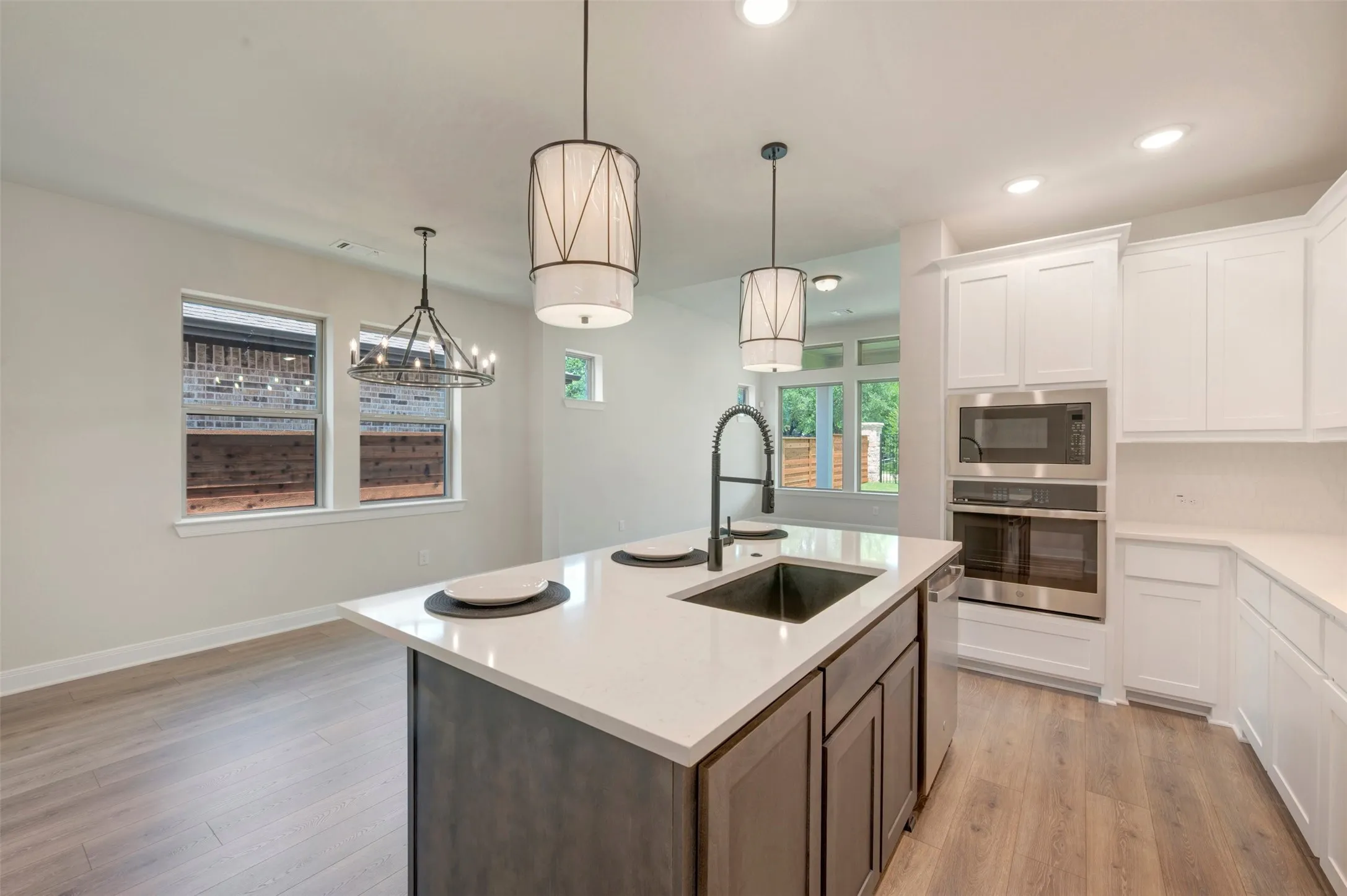 Contemporary kitchen featuring a large island with sink, white shaker cabinetry, stainless steel appliances, and wood-finish flooring