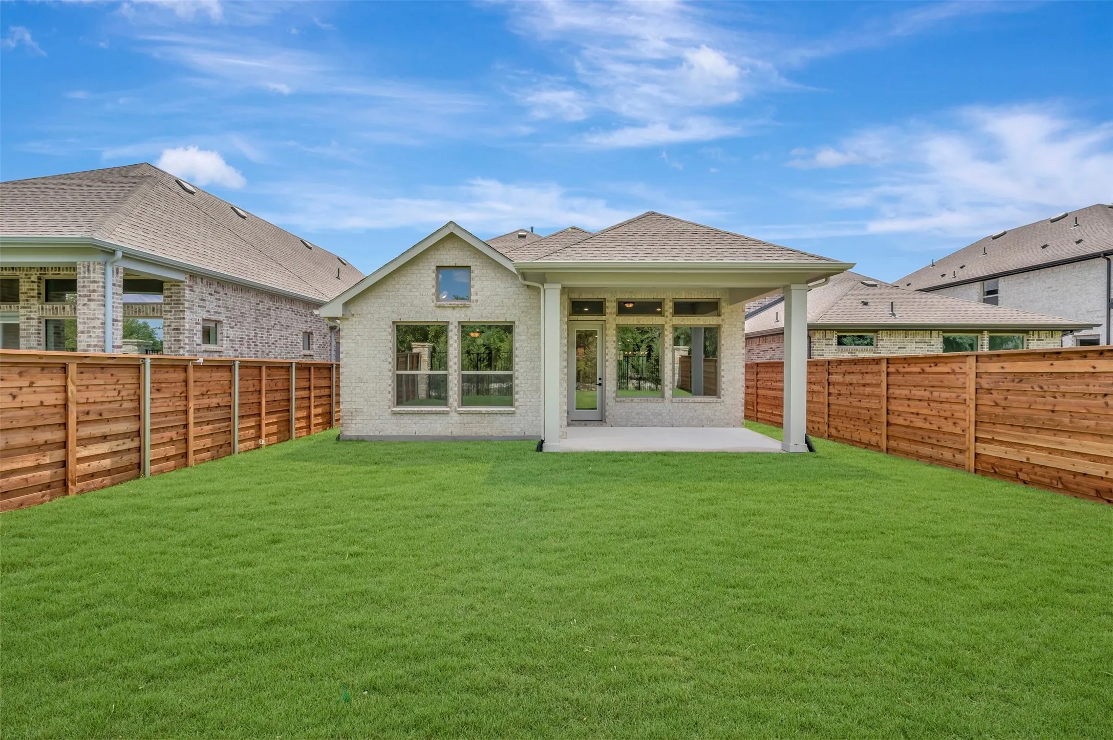 Expansive backyard oasis featuring a meticulously manicured lawn, wood-finish privacy fencing, and a modern single-story residence with covered patio area