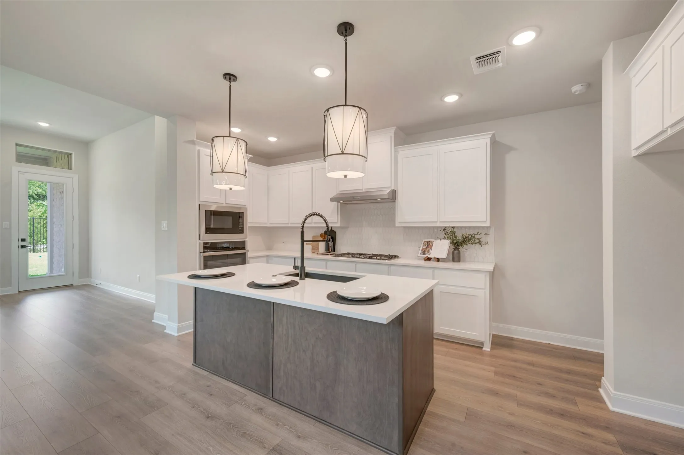 Contemporary kitchen featuring white cabinetry, a gray-stained wood-finish island with waterfall countertop edge, and stainless steel appliances