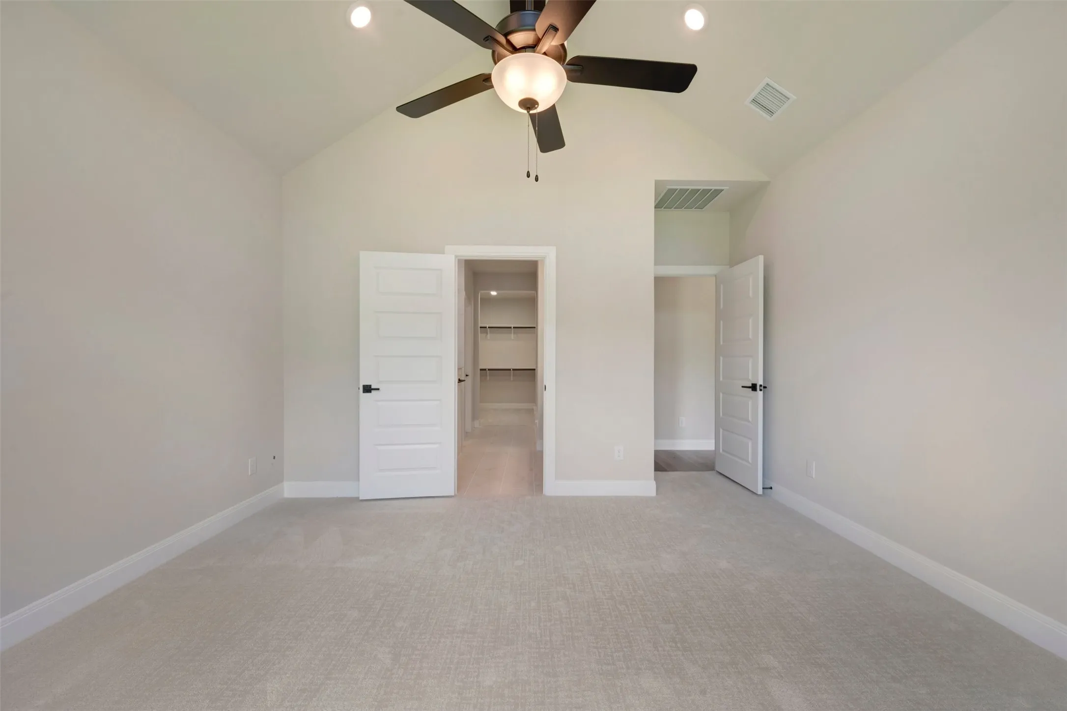 Spacious bedroom featuring neutral carpet flooring, ceiling fan with integrated lighting, and dual closet access including a walk-in closet with shelving