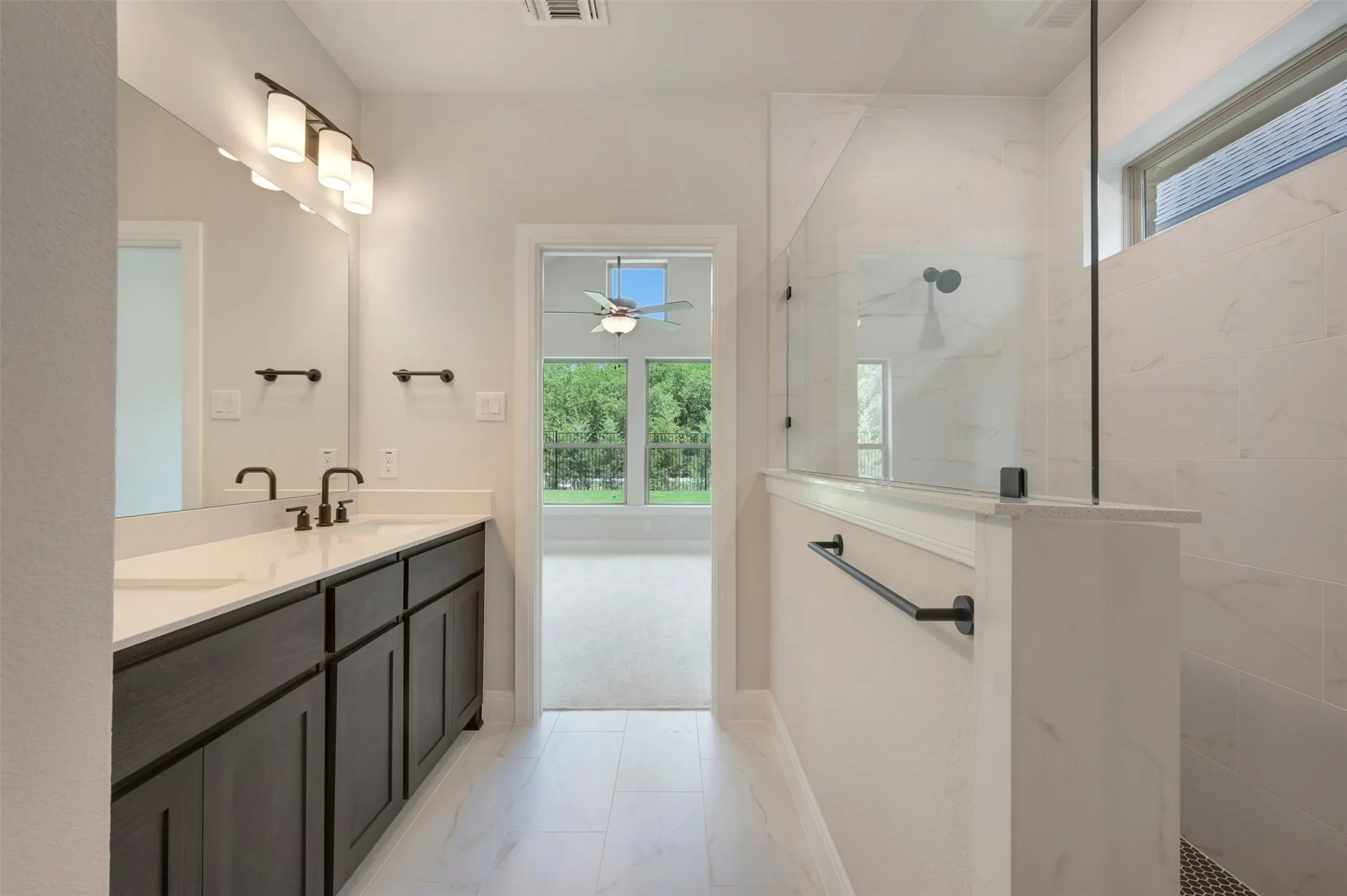 Primary Bathroom featuring a double vanity with dark cabinetry, quartz countertop, and matte black fixtures, paired with a frameless glass-enclosed walk-in shower with tile surround
