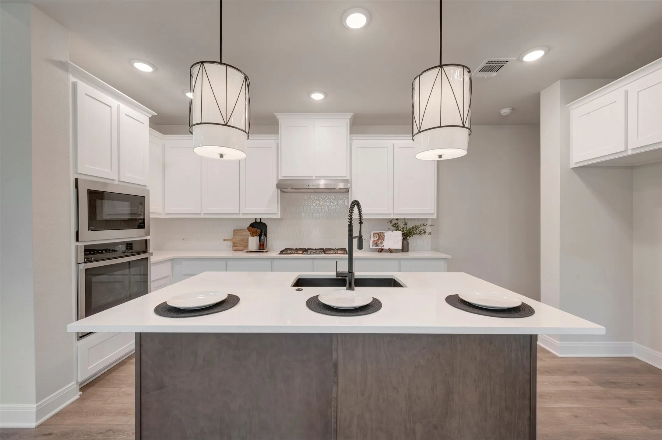 Modern kitchen featuring white cabinetry, a substantial two-tone island with wood-finish base and white quartz countertop, and stainless steel appliances including double wall ovens