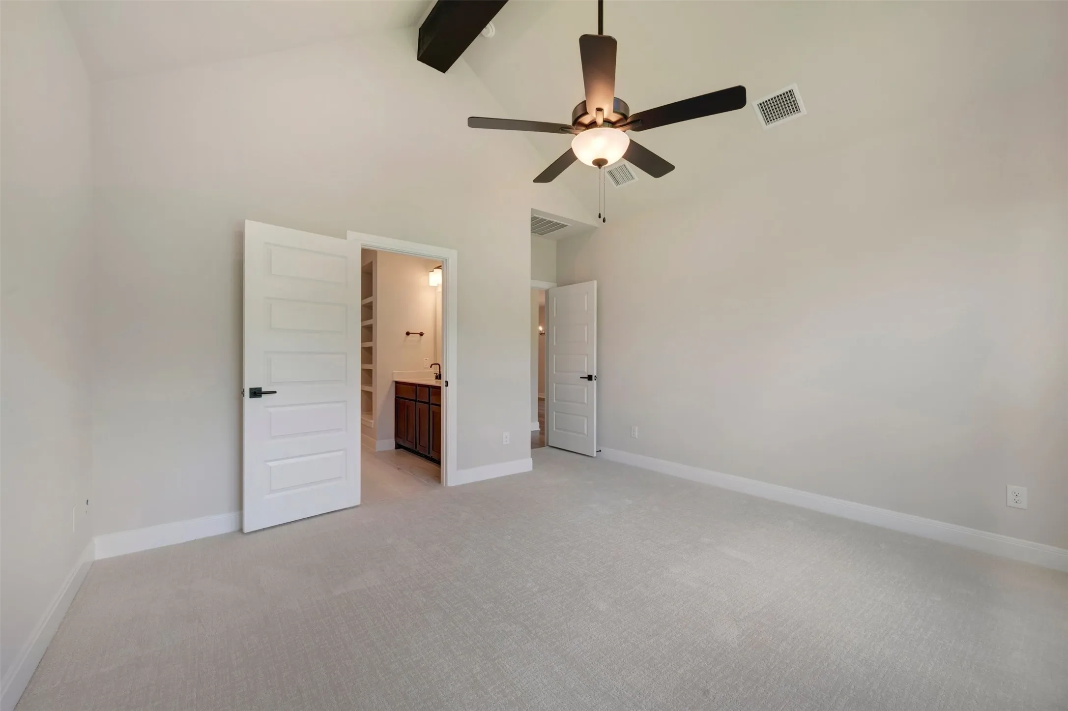 Spacious room with vaulted ceilings and a ceiling fan, featuring plush light-toned carpeting, crisp white baseboards, and neutral wall paint