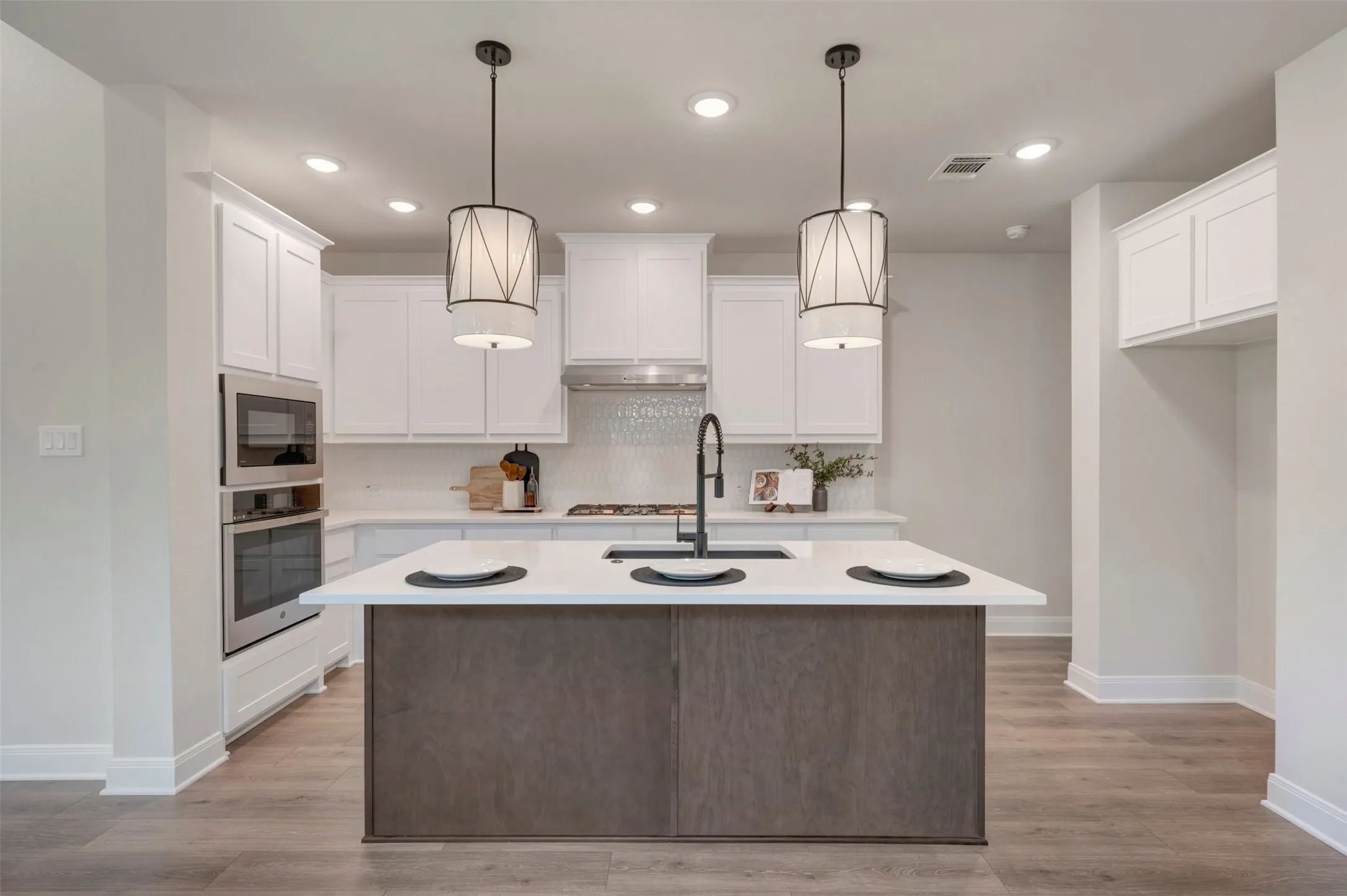 Modern kitchen featuring a two-tone design with white cabinetry, a dark wood-finish island with waterfall countertop, and stainless steel appliances including dual wall-mounted ovens