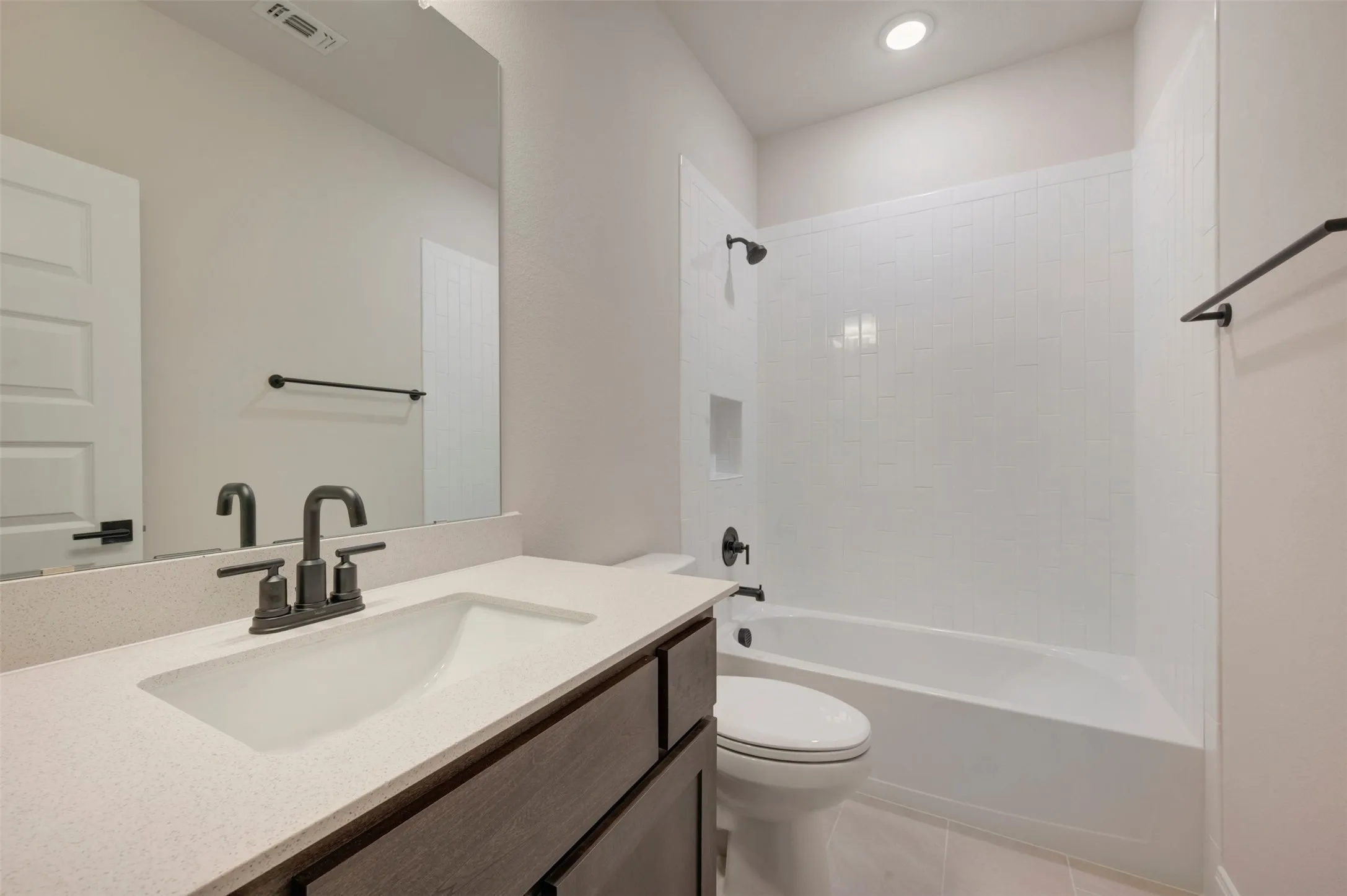 Bathroom featuring a wood-finish vanity with a light-toned countertop, an integrated sink, and dark-finish fixtures
