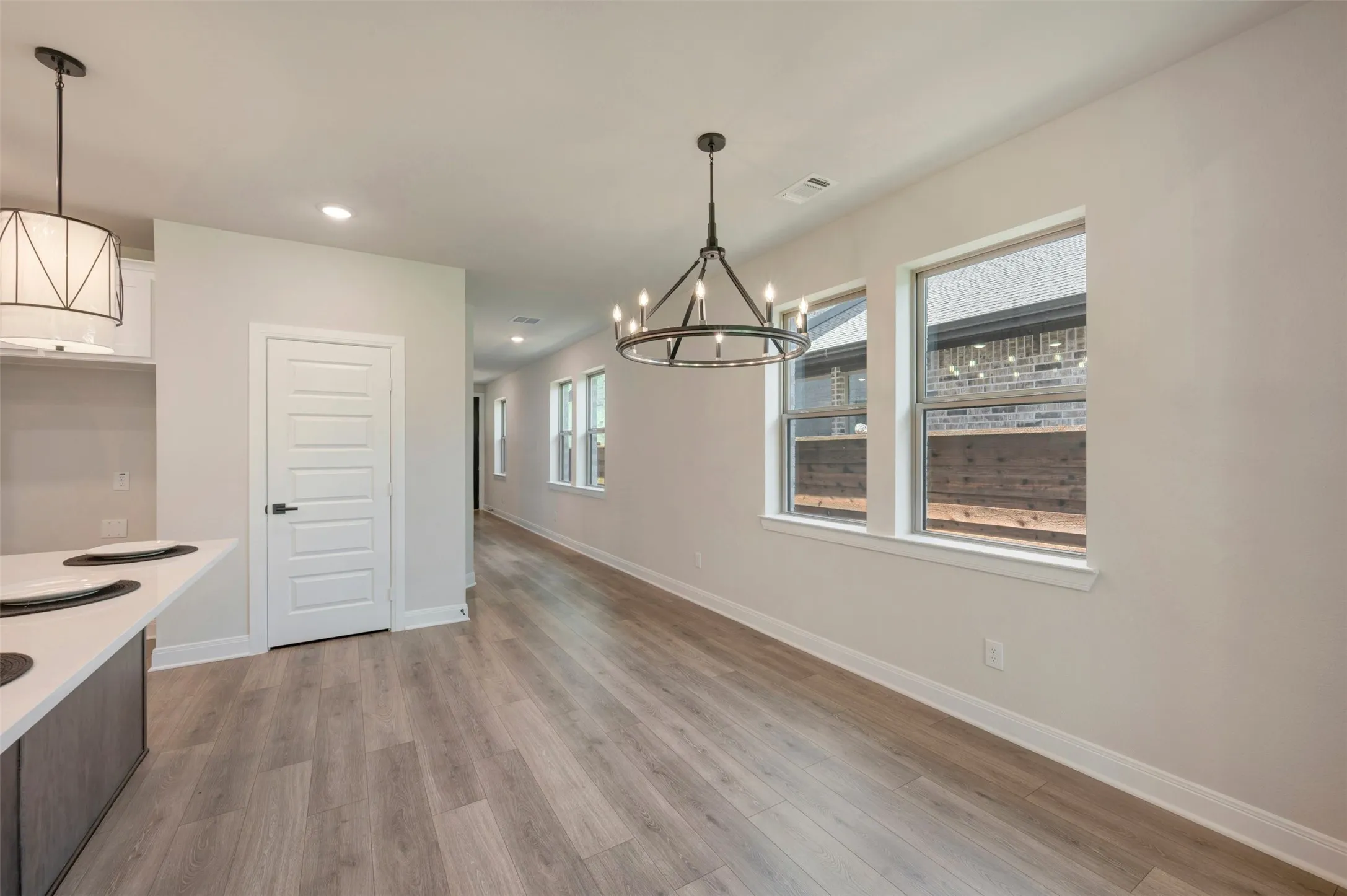 Spacious open-concept area featuring wood-finish flooring, a modern linear chandelier, and multiple windows