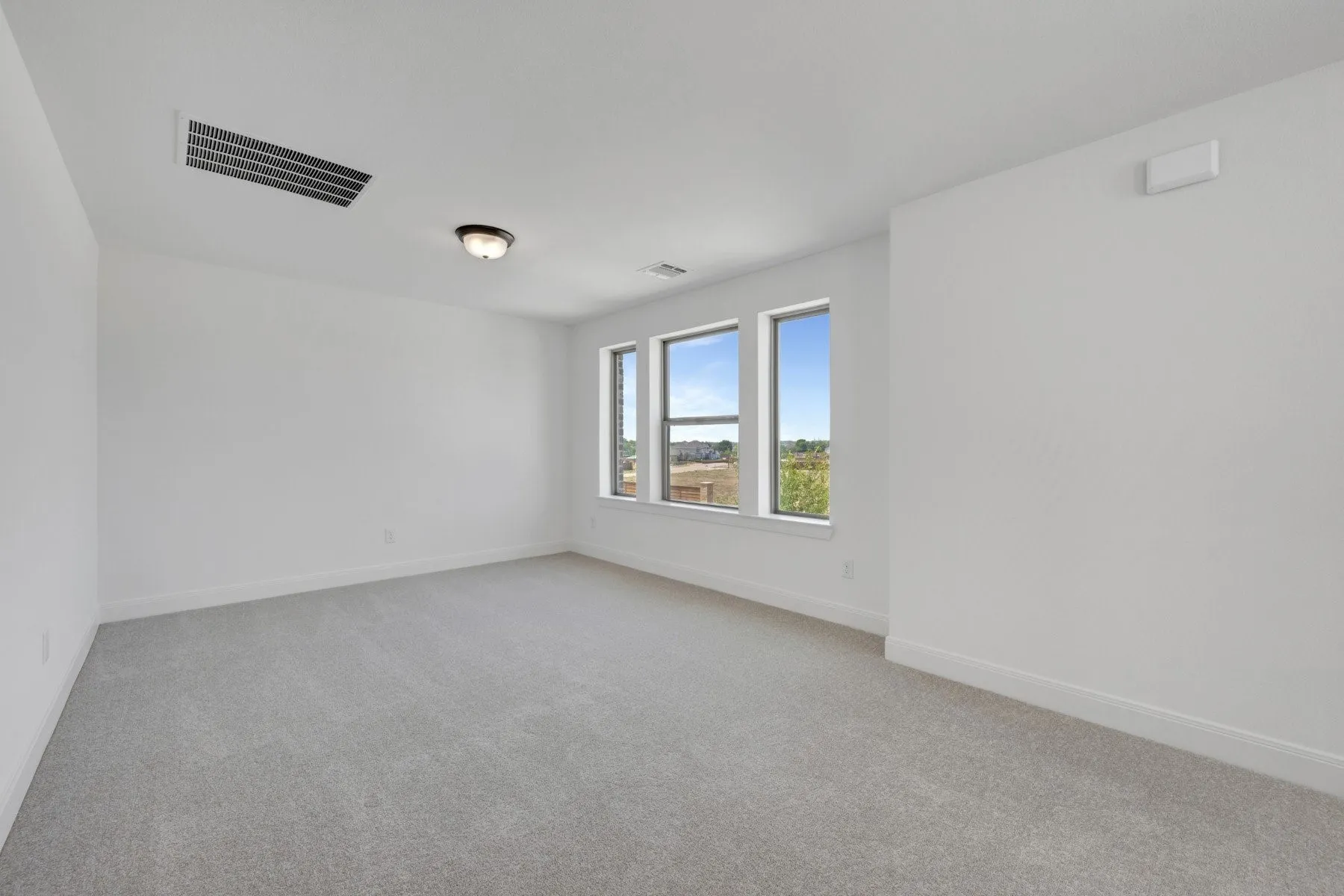 Spacious room featuring three vertical windows, light grey carpet, white walls, white baseboards, and a flush mount ceiling light