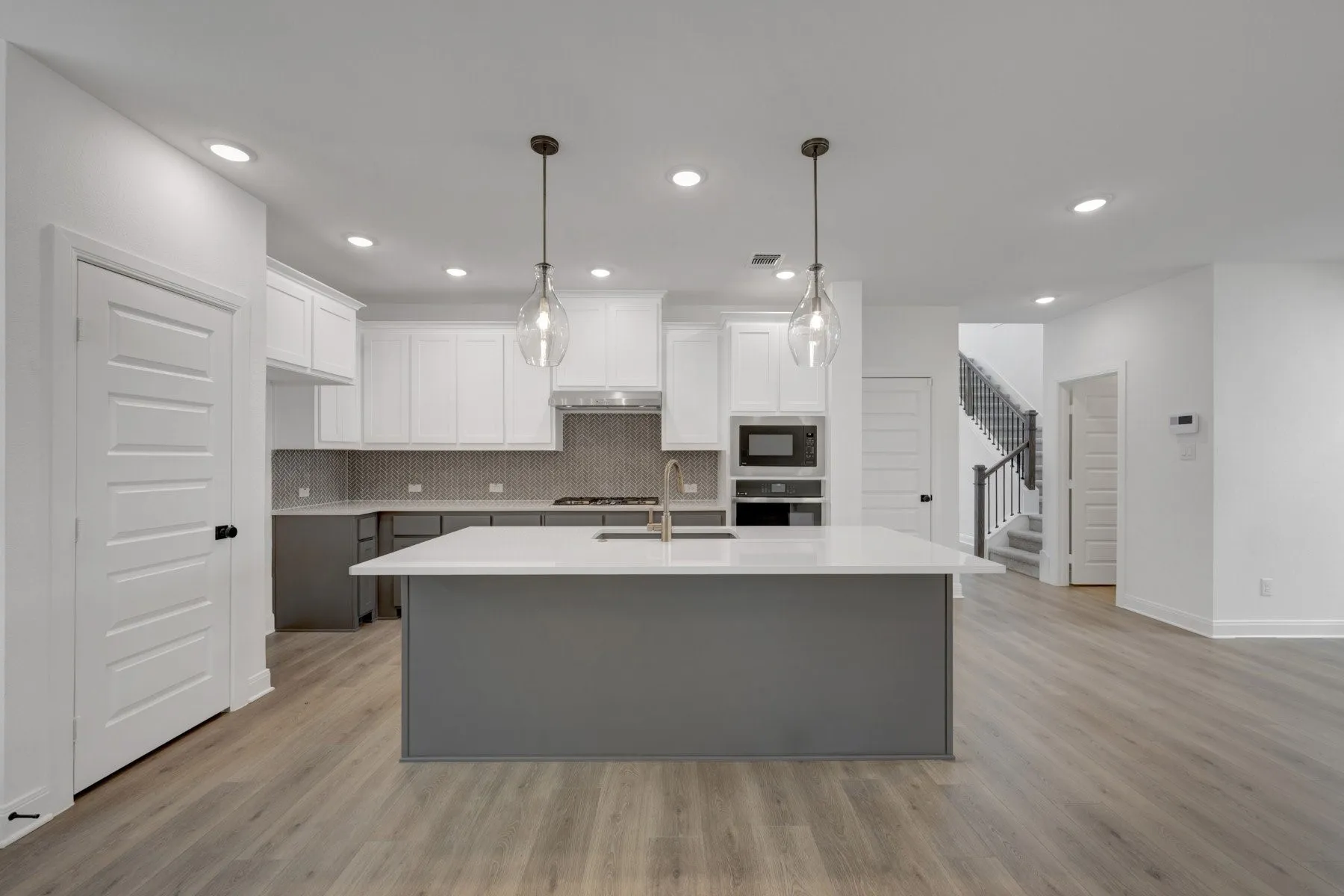 Open-concept kitchen featuring a spacious island with a light-toned countertop, two-tone cabinetry with white uppers and gray lowers, stainless steel appliances, and a tiled backsplash