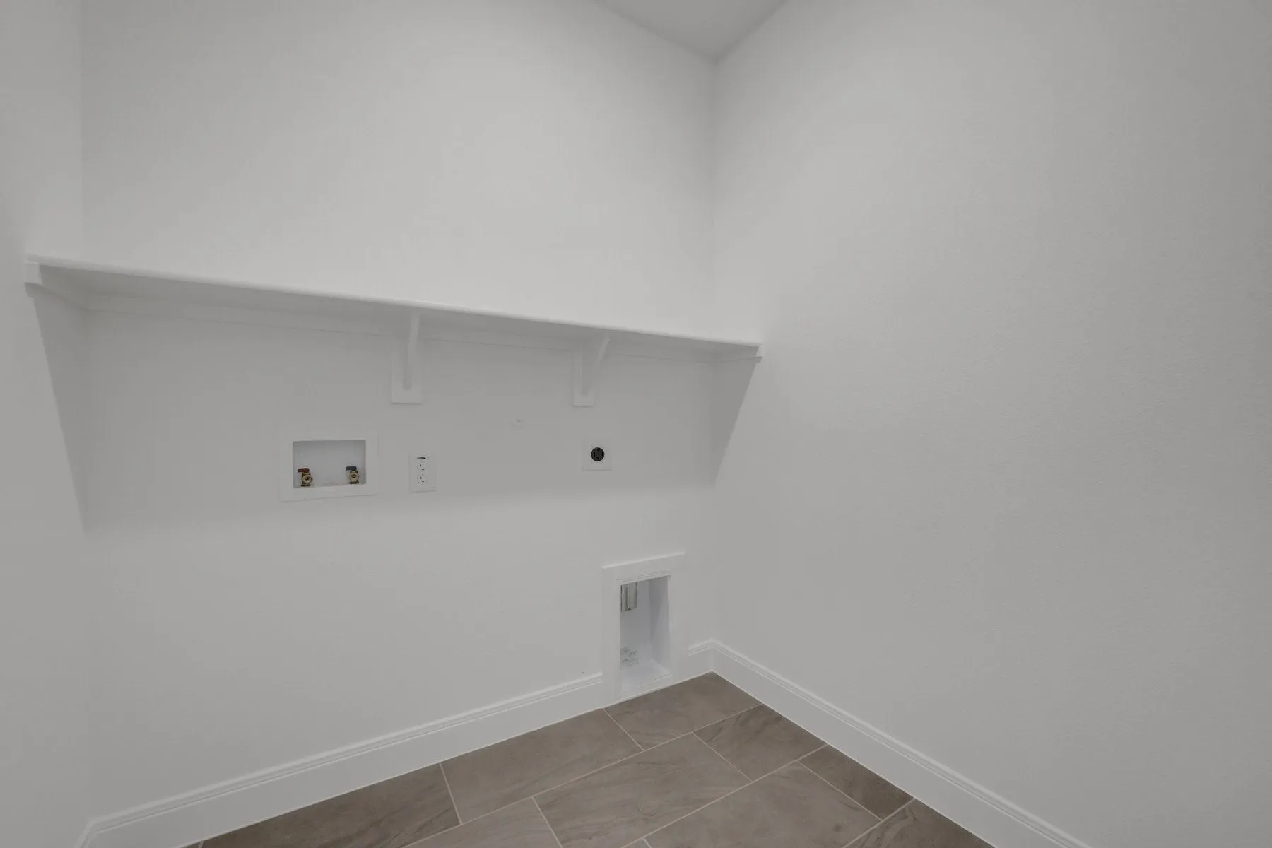 Dedicated laundry space featuring a white wall shelf, utility hookups, and tiled flooring