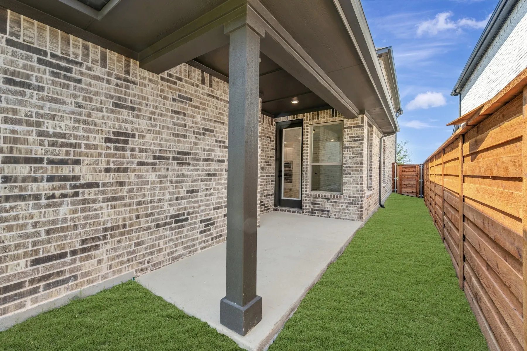 Covered patio with a concrete surface, brick exterior, and a solid wood privacy fence