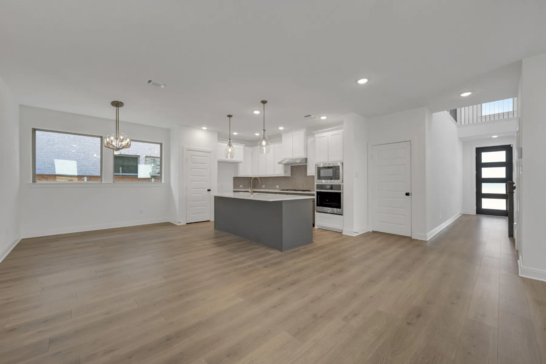 Open-concept living area featuring wood-finish flooring, recessed lighting, and a modern kitchen with a gray island and stainless steel appliances