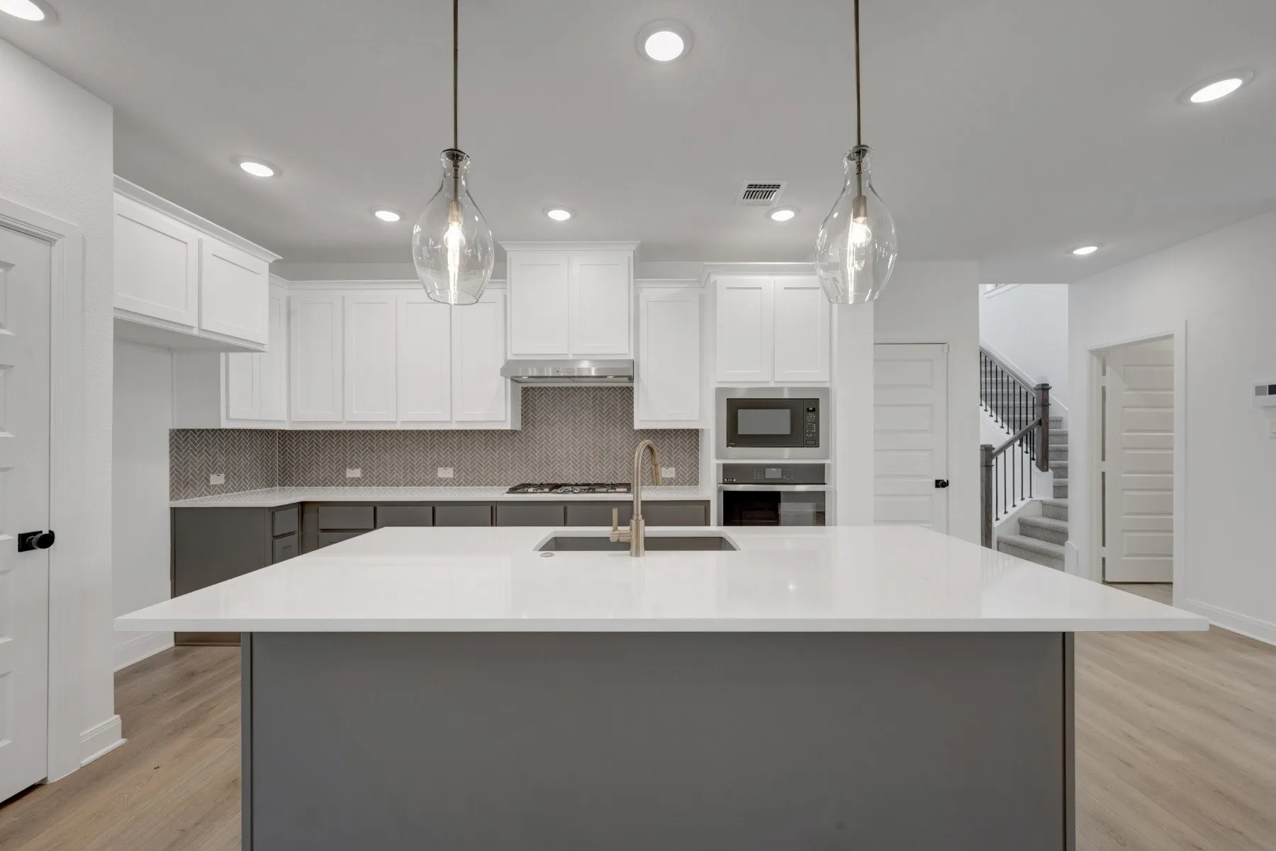 Kitchen featuring a large central island with a white countertop and undermount sink, two-tone cabinetry, mosaic tile backsplash, and wood-finish flooring