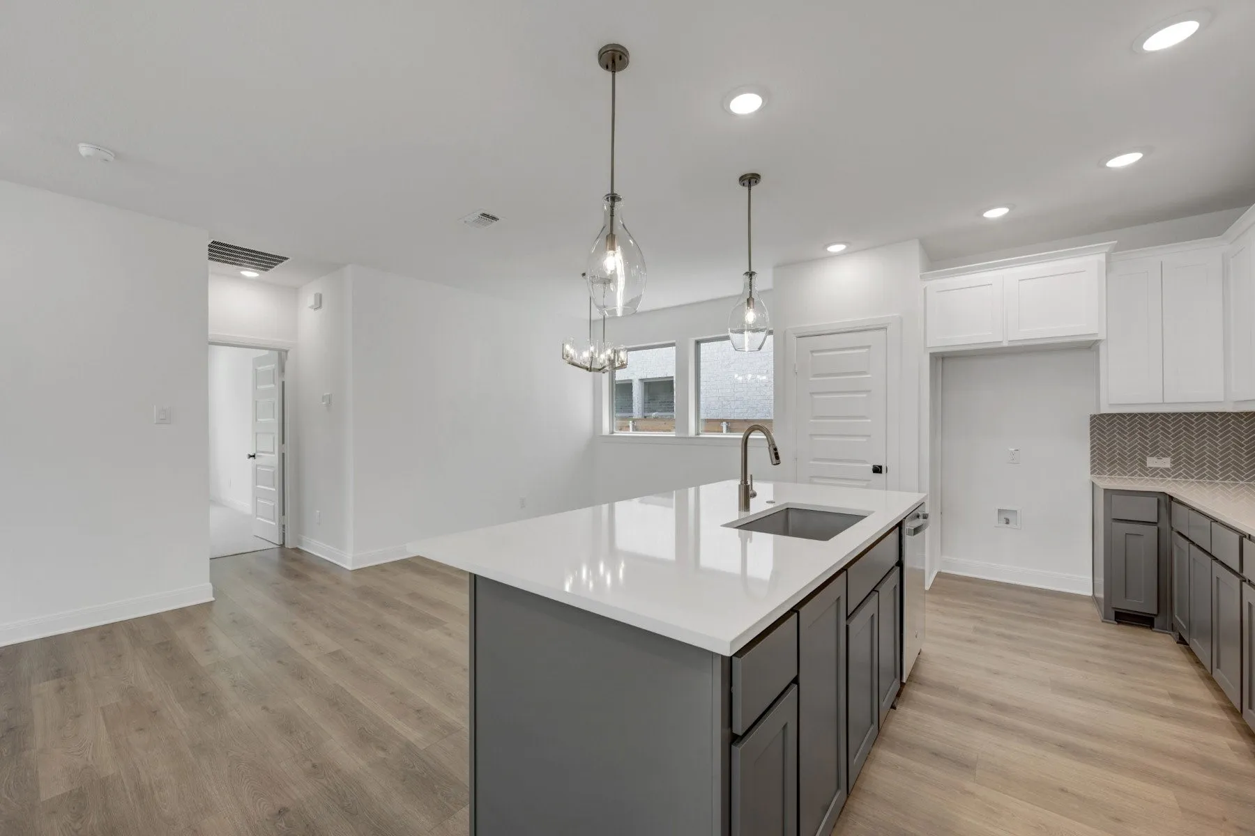 Modern kitchen featuring a large island with white countertop, undermount sink, and grey cabinetry