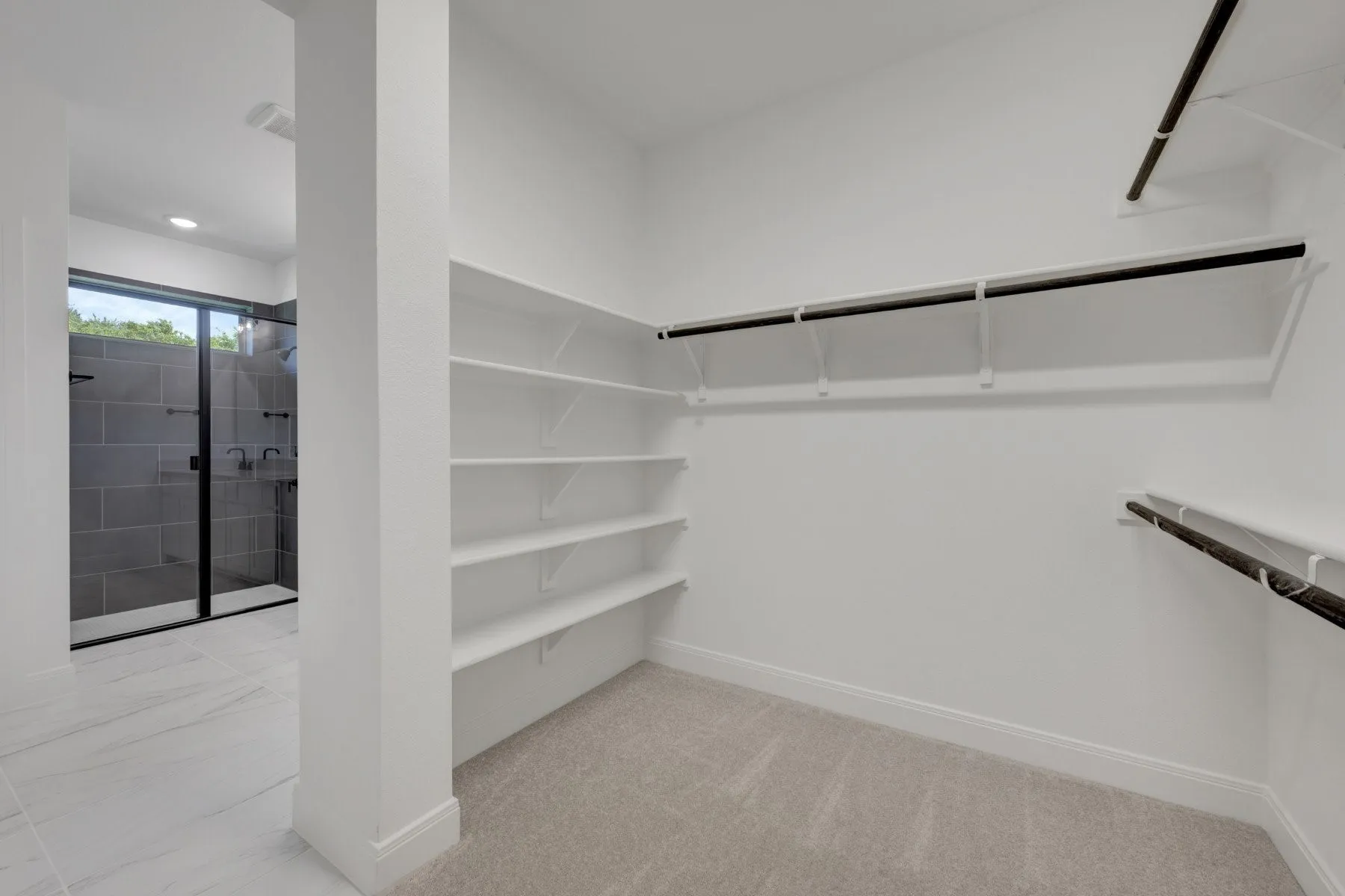 Primary Walk-In Closet featuring built-in shelving along two walls, a black metal hanging rod system, recessed ceiling lighting, and neutral carpeting