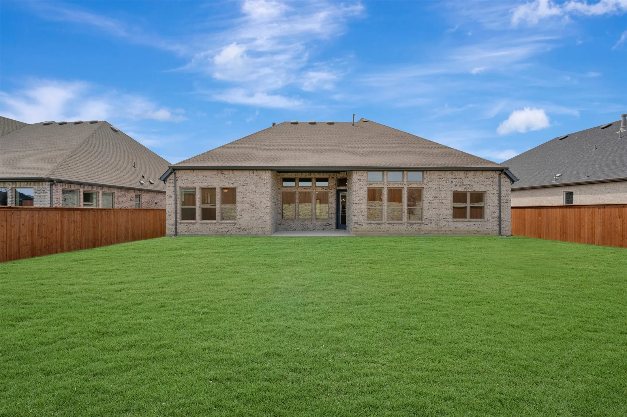 Expansive backyard featuring a lush lawn, privacy fencing, a brick exterior, a covered patio, and multiple windows