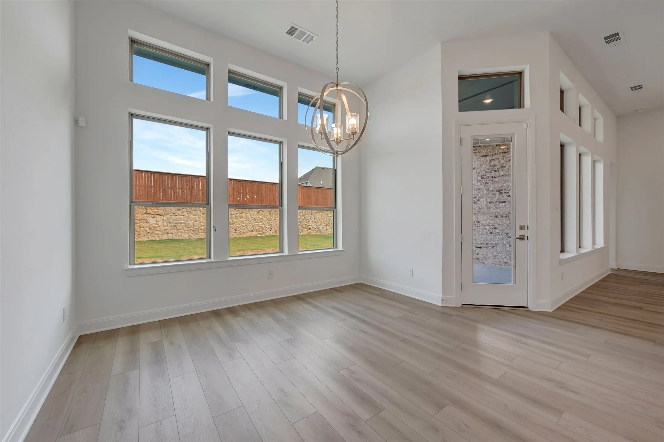 Vaulted ceiling with a chandelier, extensive window array, wood-finish flooring, white trim, and a glass-paneled door