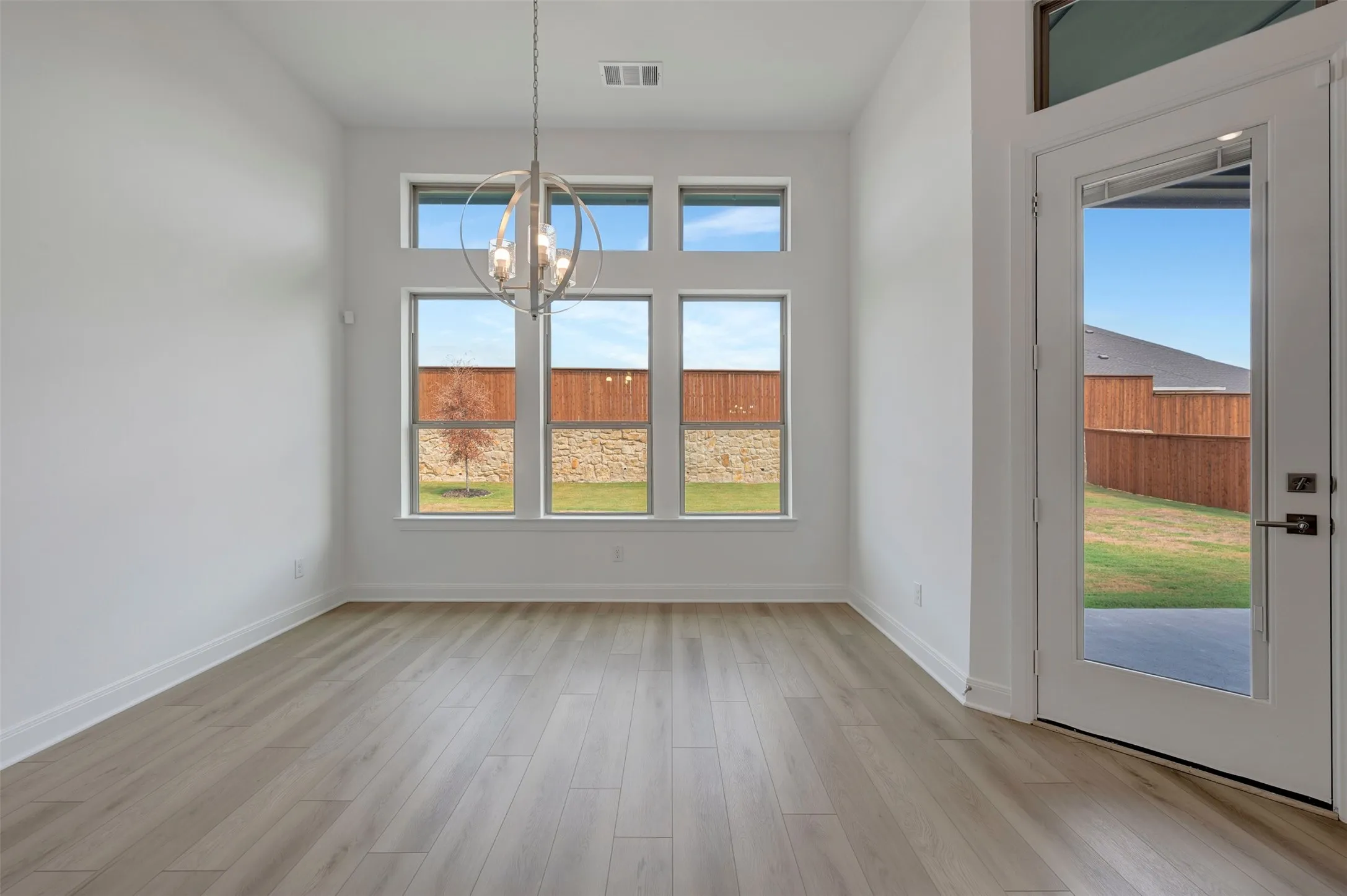 Spacious room featuring wood-finish flooring, high ceilings, a contemporary chandelier, and a glass-paneled door