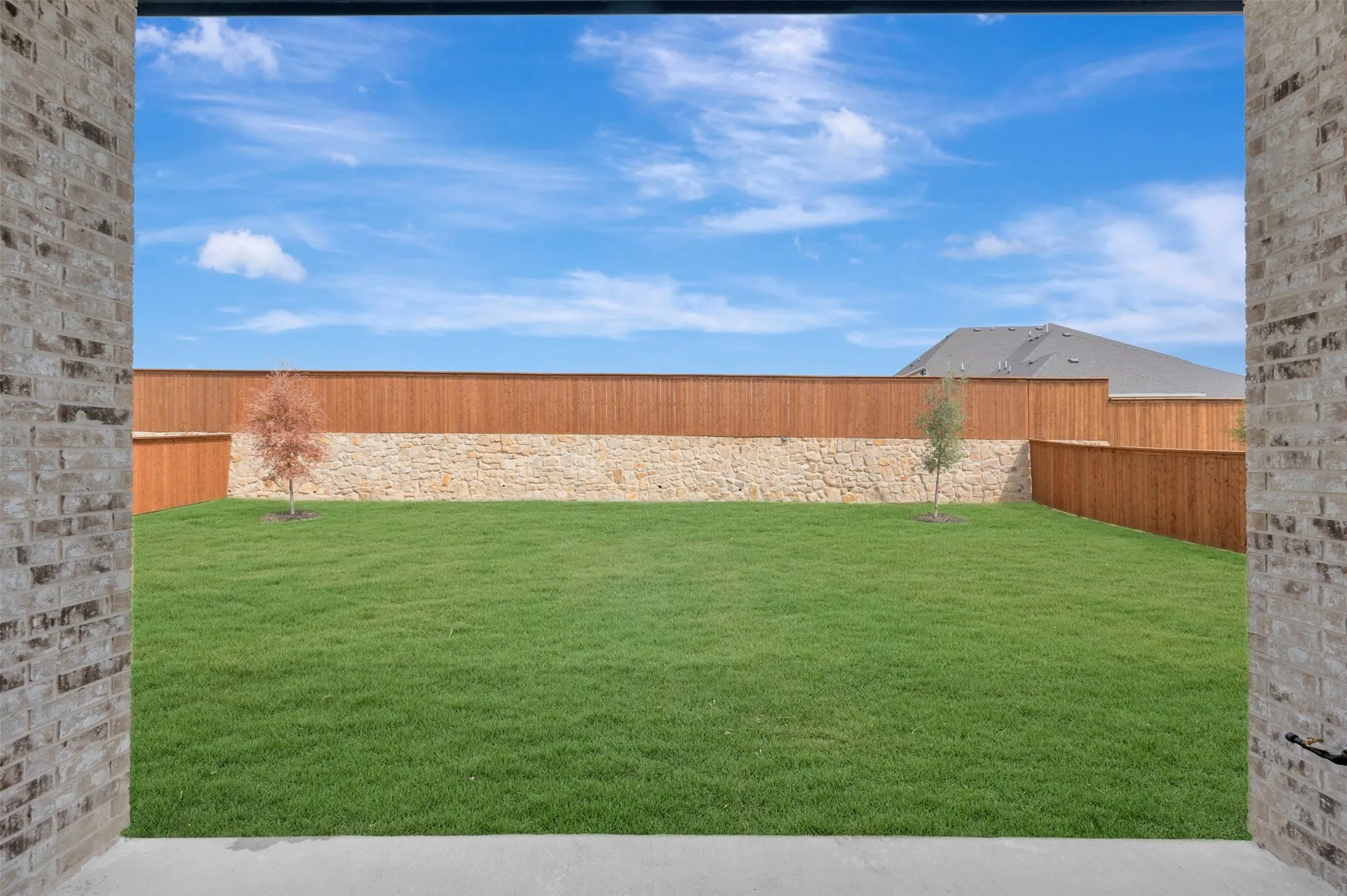 Expansive lawn area with a stone and wood privacy fence, featuring two young trees