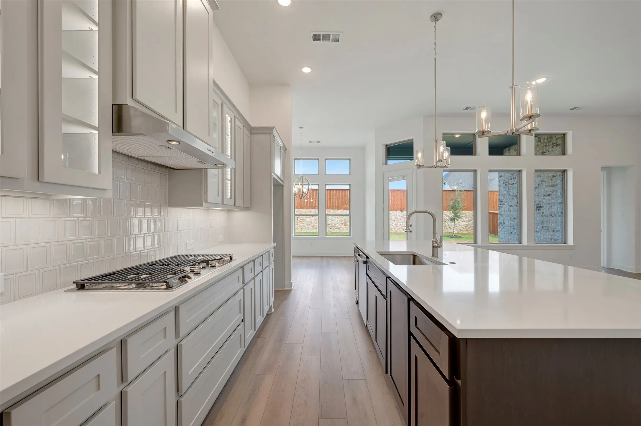 Kitchen featuring light grey cabinetry, white subway tile backsplash, a gas cooktop, and an expansive center island with an undermount sink and pendant lighting