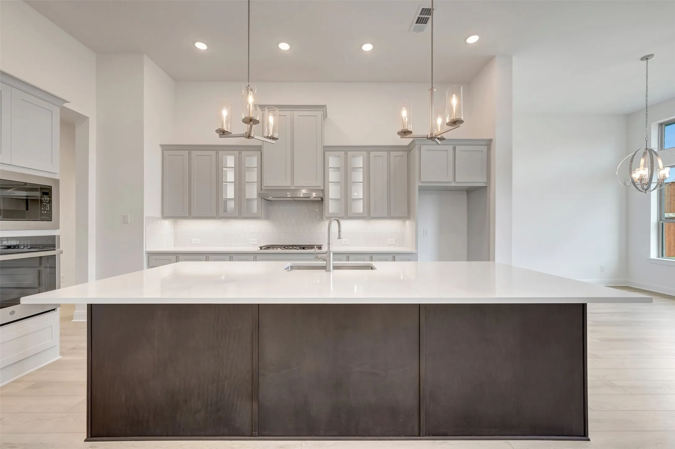 Kitchen featuring a large island with white countertop, light grey cabinetry, built-in stainless steel appliances, and wood-finish flooring