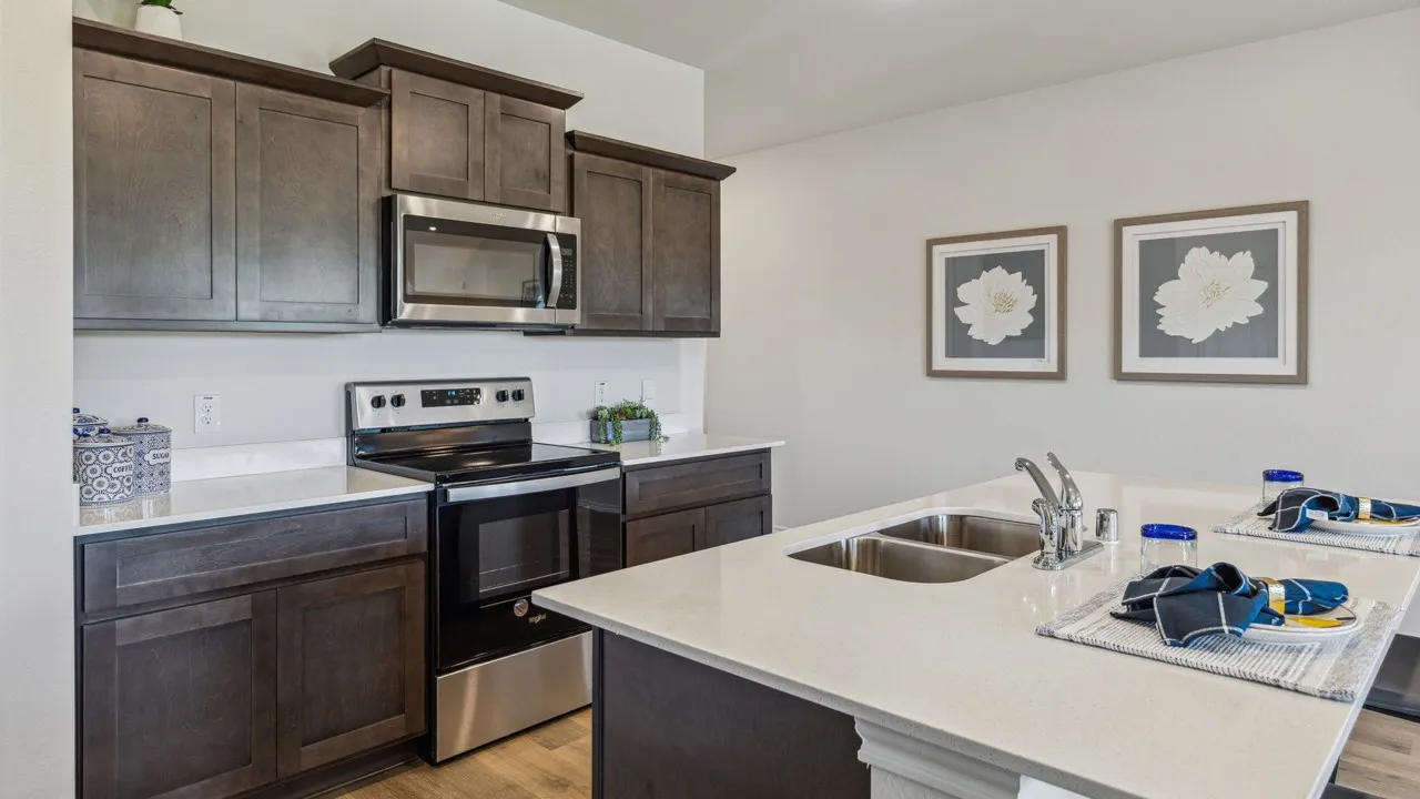 Kitchen featuring stainless steel appliances, dark wood finish cabinets, a kitchen island with sink, and light stone countertops