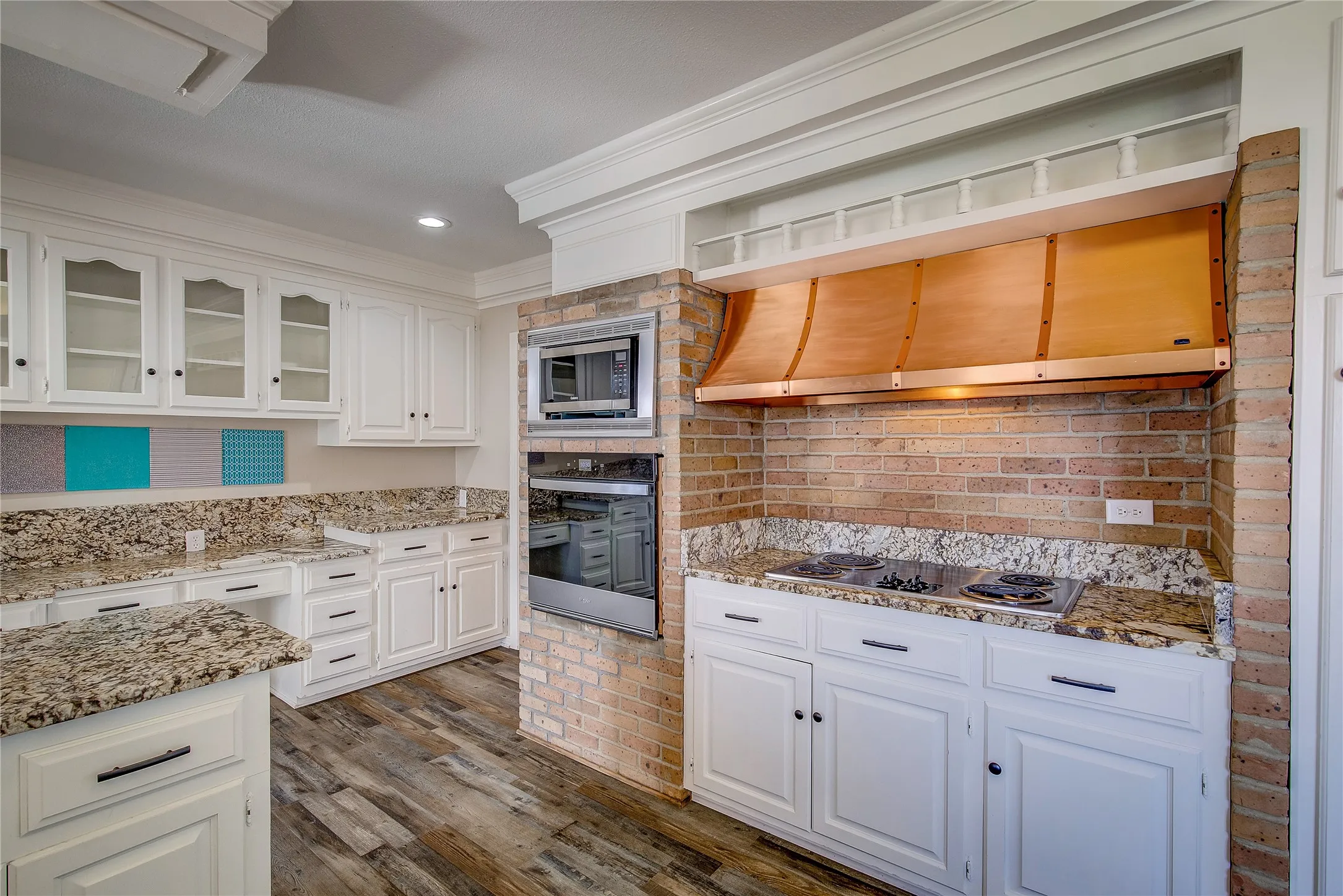 Kitchen has electric cooktop with copper vent hood and storage above; wall oven and microwave, all built into brick