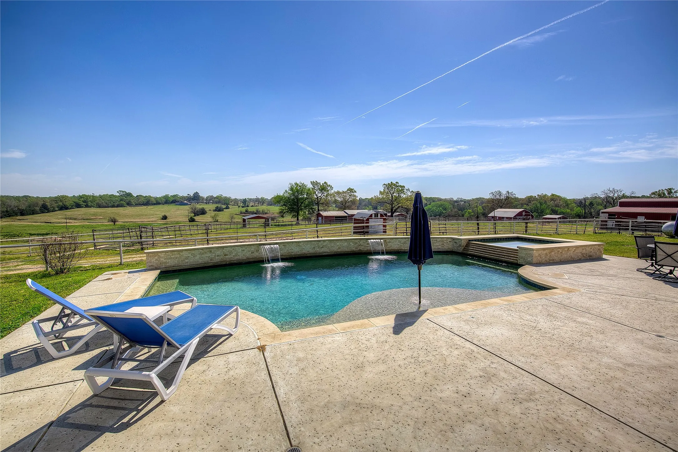 Another view of pool and hot tub, with barns and pastures beyond.