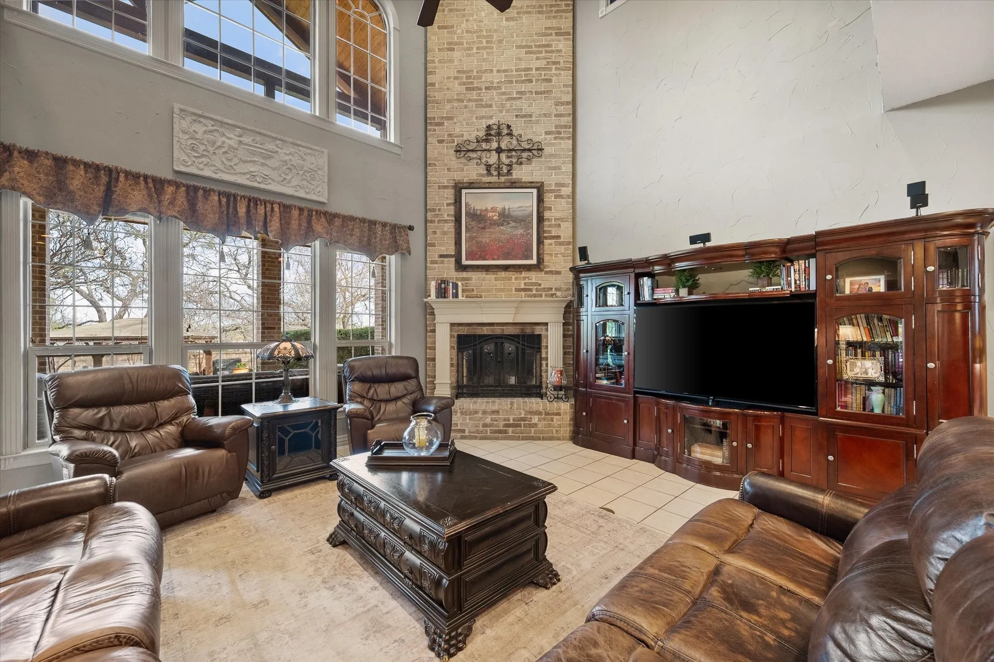 Living room with light tile patterned floors, a ceiling fan, a brick fireplace, and a high ceiling