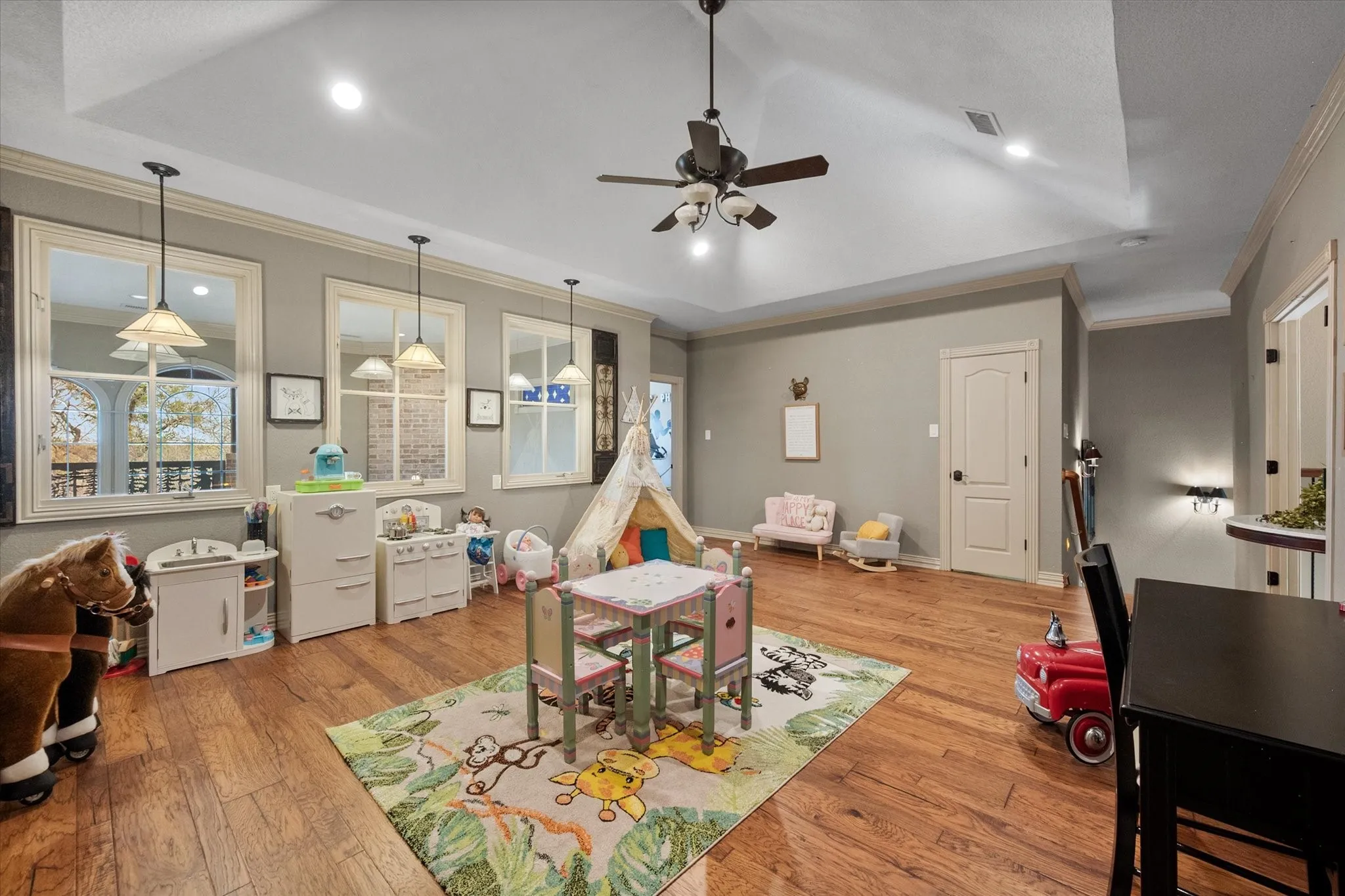 Playroom with crown molding, ceiling fan, light wood-style floors, and a tray ceiling