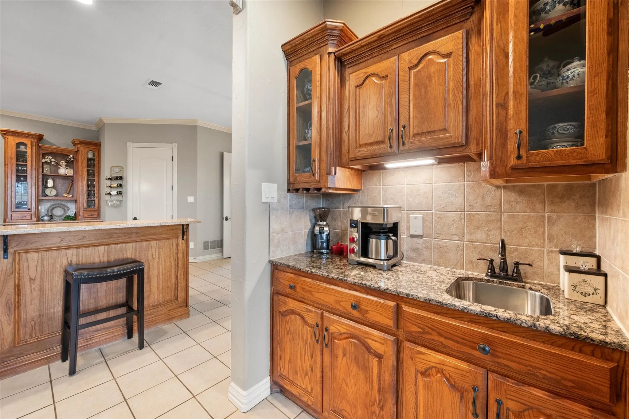 Kitchen featuring glass fronted cabinets, wood finish cabinets, light stone countertops, crown molding, and light tile patterned floors