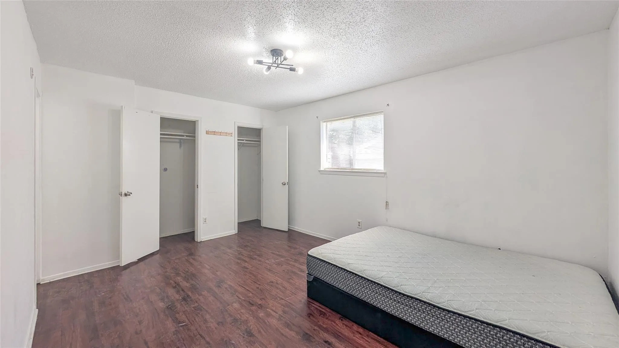 Bedroom with two closets, dark wood-style flooring, and a textured ceiling