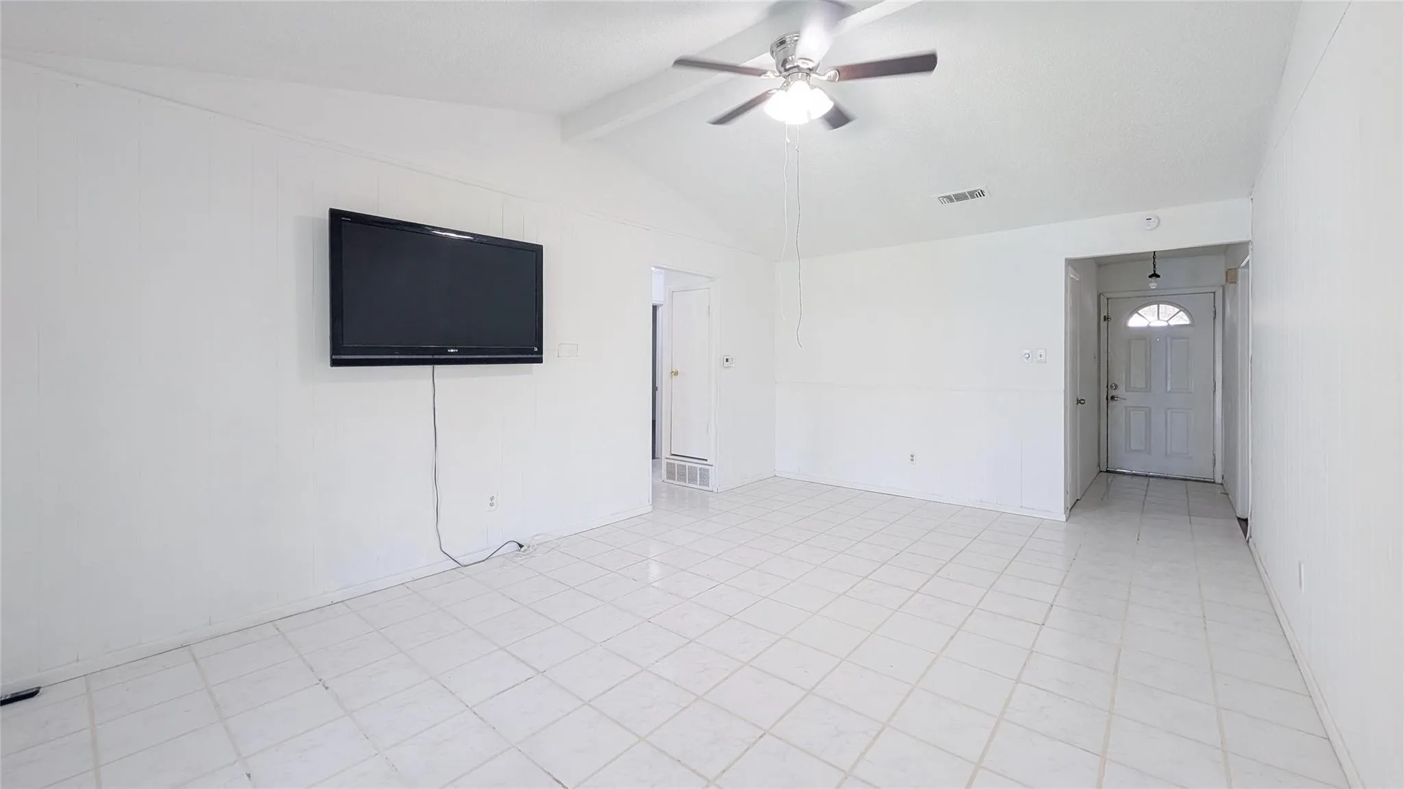 Empty room featuring a ceiling fan, beam ceiling, and light tile patterned floors