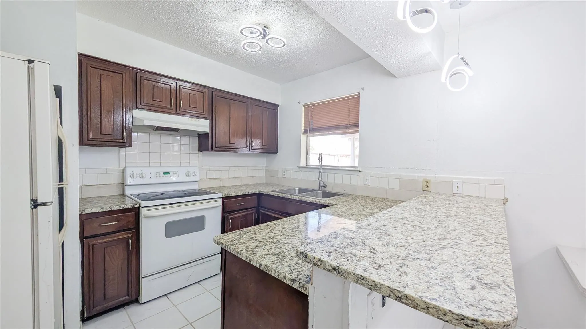 Kitchen with white appliances, a textured ceiling, dark wood finish cabinetry, a peninsula, and backsplash
