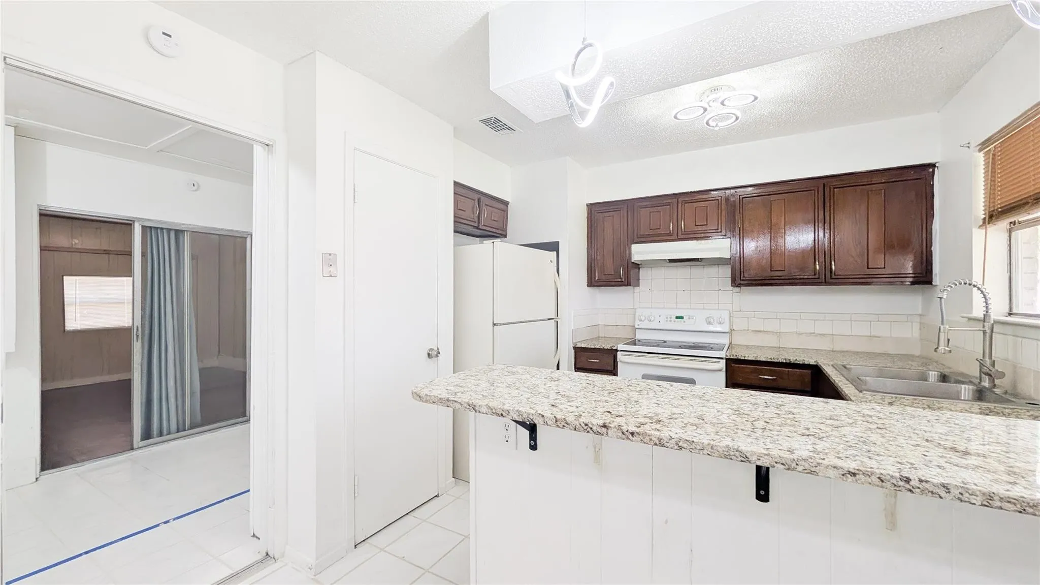 Kitchen with white appliances, dark wood finish cabinetry, decorative backsplash, a peninsula, and a kitchen bar
